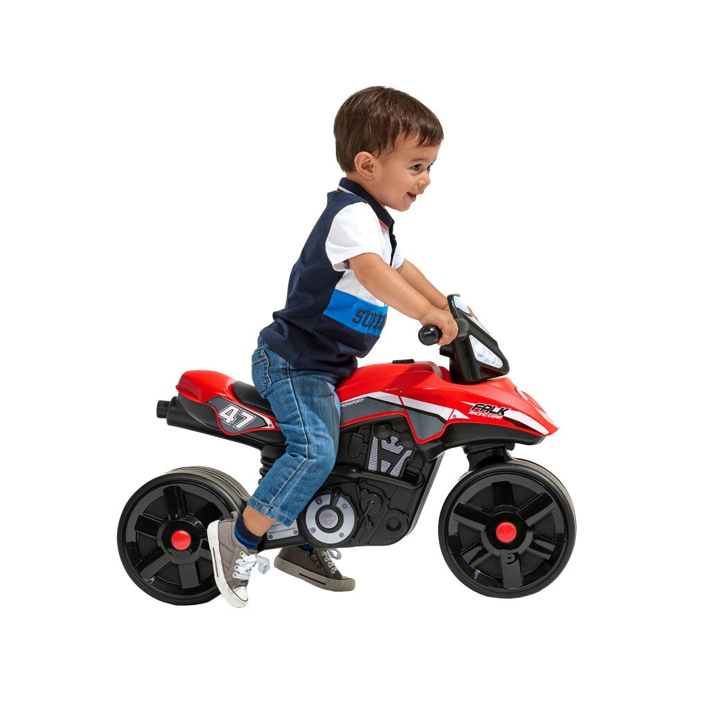 Ein kleiner Junge fährt auf einem rot-schwarzen Spielzeugmotorrad vor weißem Hintergrund.