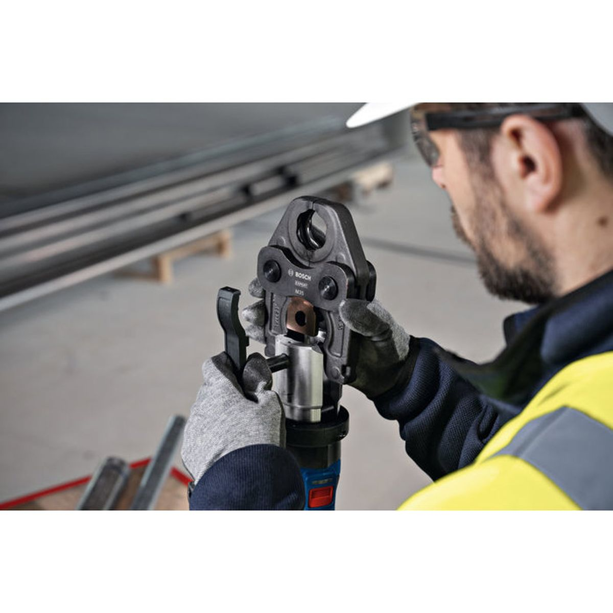 Ein Arbeiter in Schutzkleidung bedient ein Bosch-Presswerkzeug an einem Metallrohr.