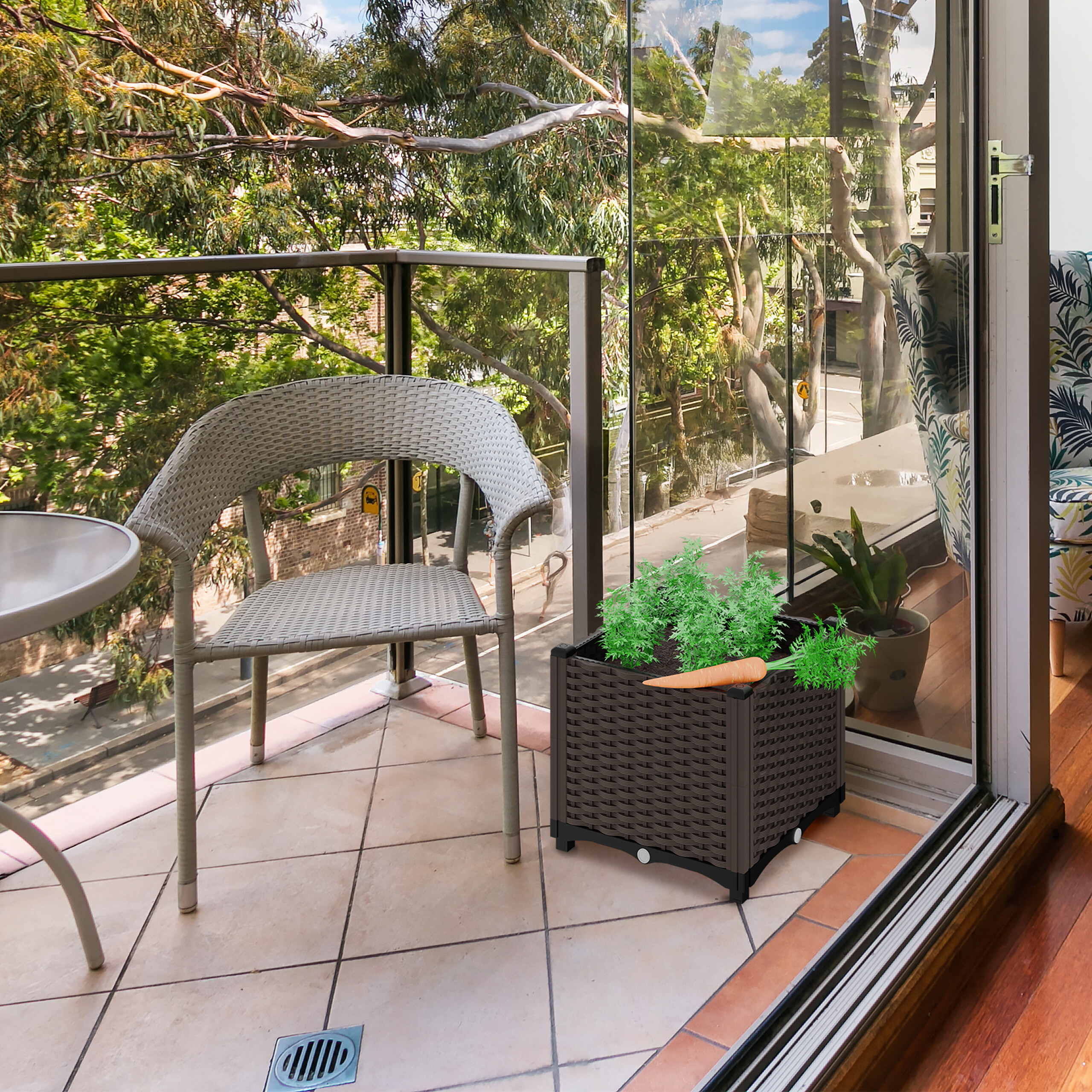 Sonniger Balkon mit Rattanstuhl, Tisch und Pflanzkasten mit Karotten, Blick auf begrünte Bäume.