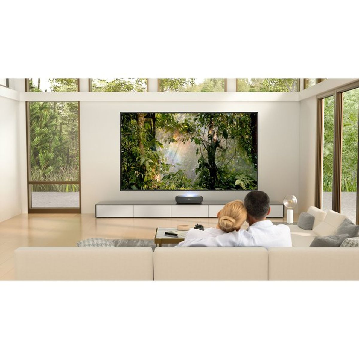 Ein Paar sitzt auf einem Sofa und schaut auf einen großen Bildschirm mit Waldbild.