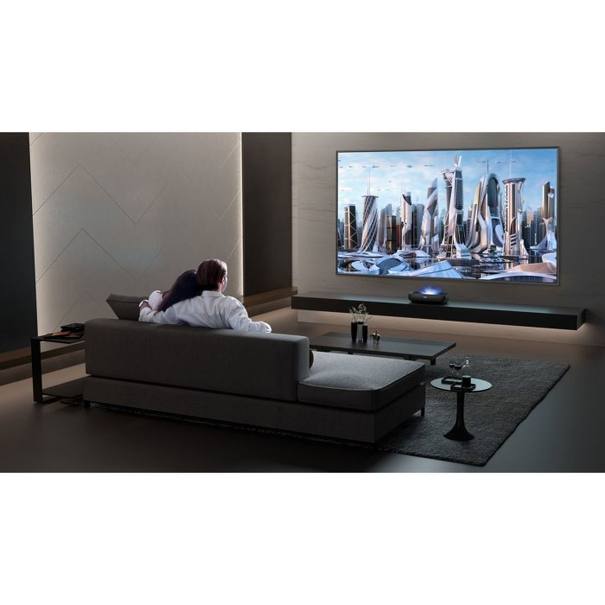 Ein Paar sitzt auf einem grauen Sofa in einem modernen Wohnzimmer und schaut auf einen großen Bildschirm mit einer futuristischen Stadt.