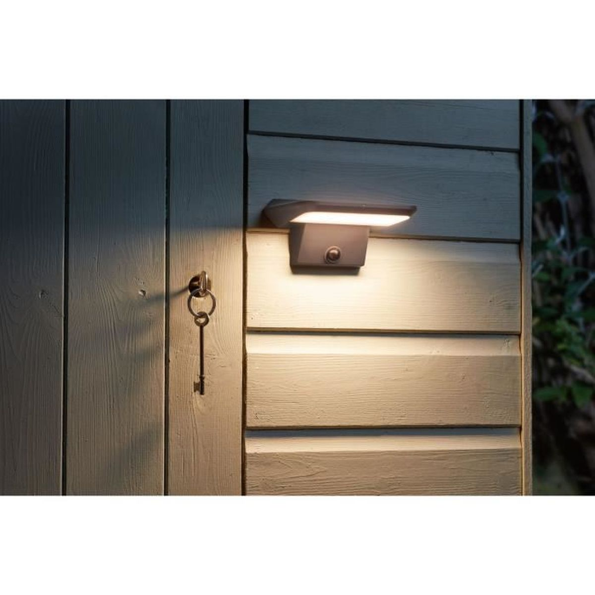Eine Solar-Wandleuchte leuchtet an einer Holzwand nahe einer alten Schlüsselloch-Tür.
