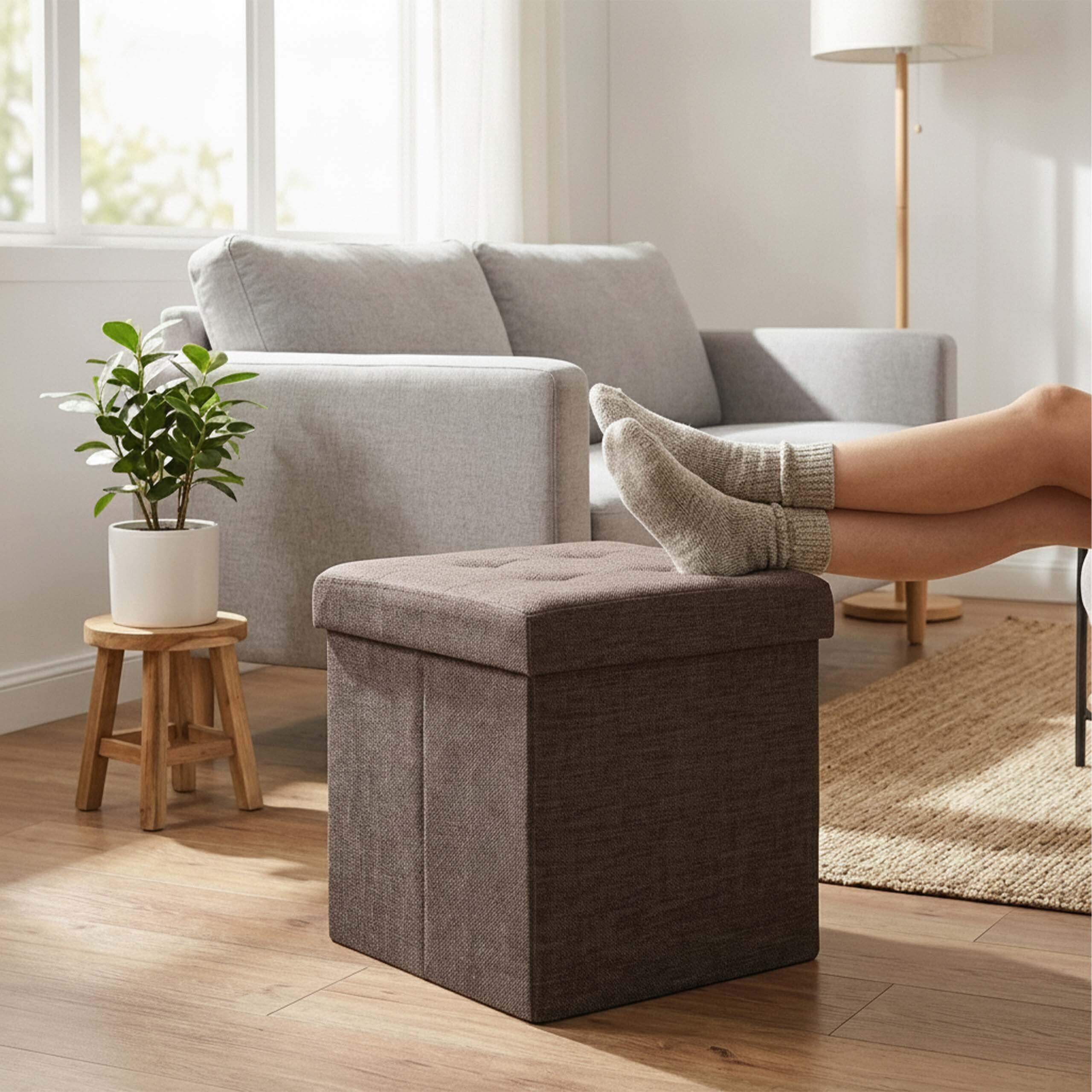 Beine in Socken liegen auf einem braunen Hocker in einem Wohnzimmer mit grauer Couch.