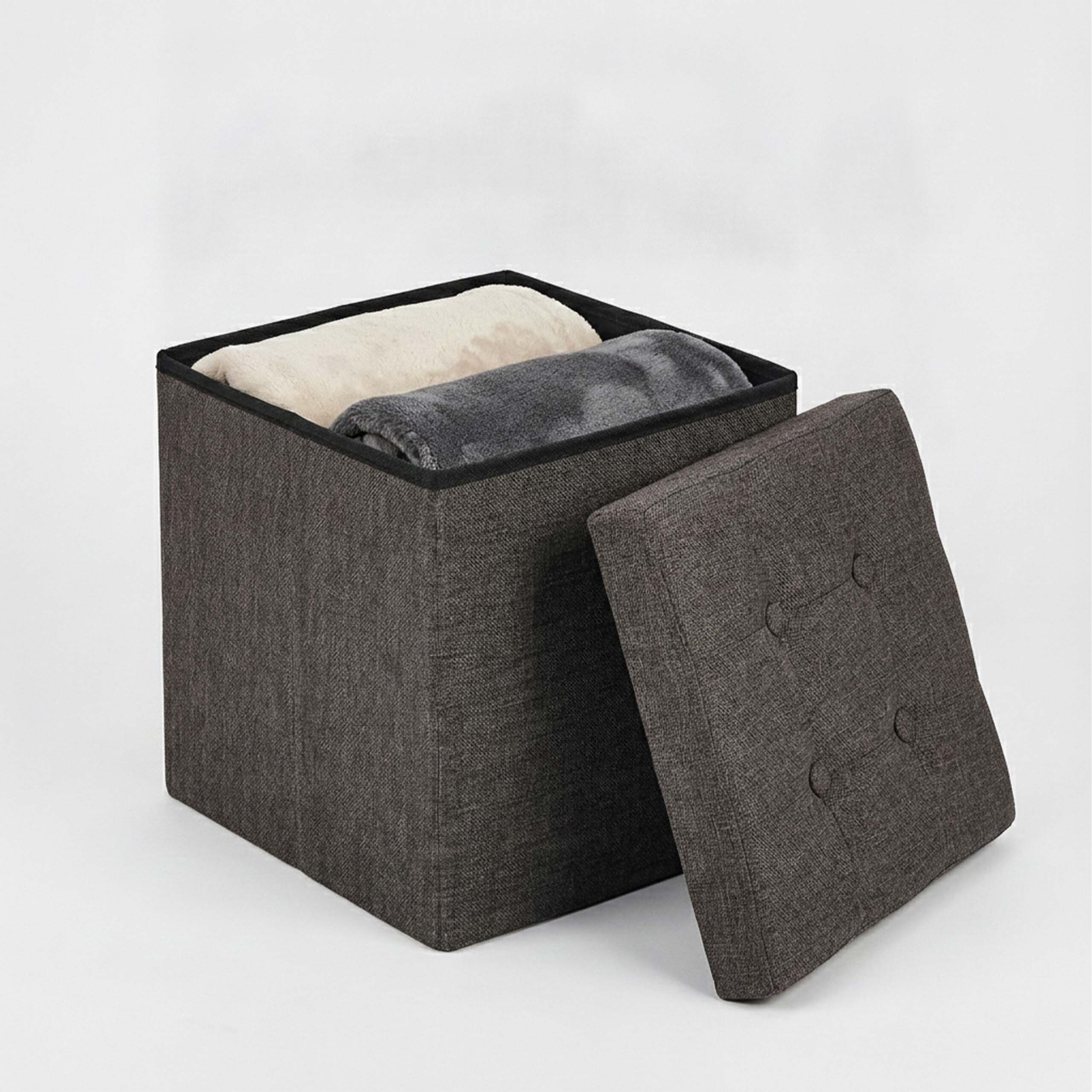 Dunkelgrauer Stoffhocker mit Stauraum, gefüllt mit gerollten Decken und abgenommenem Deckel.