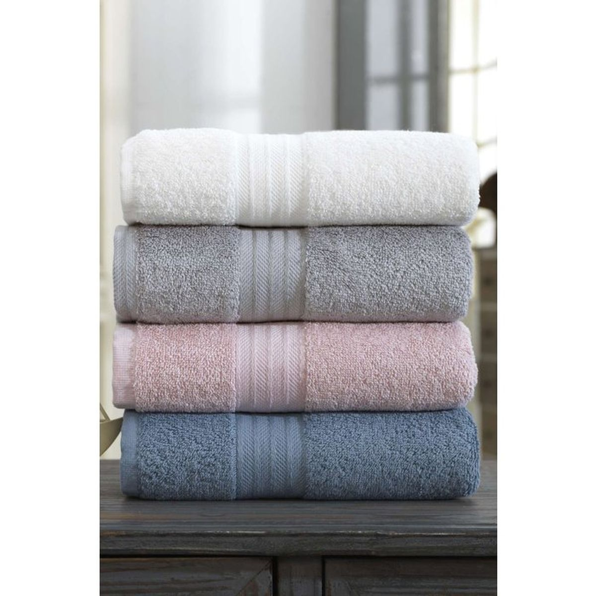Ein Stapel aus vier unterschiedlich farbigen Handtüchern in weiß, grau, rosa und blau auf einem Holztisch.