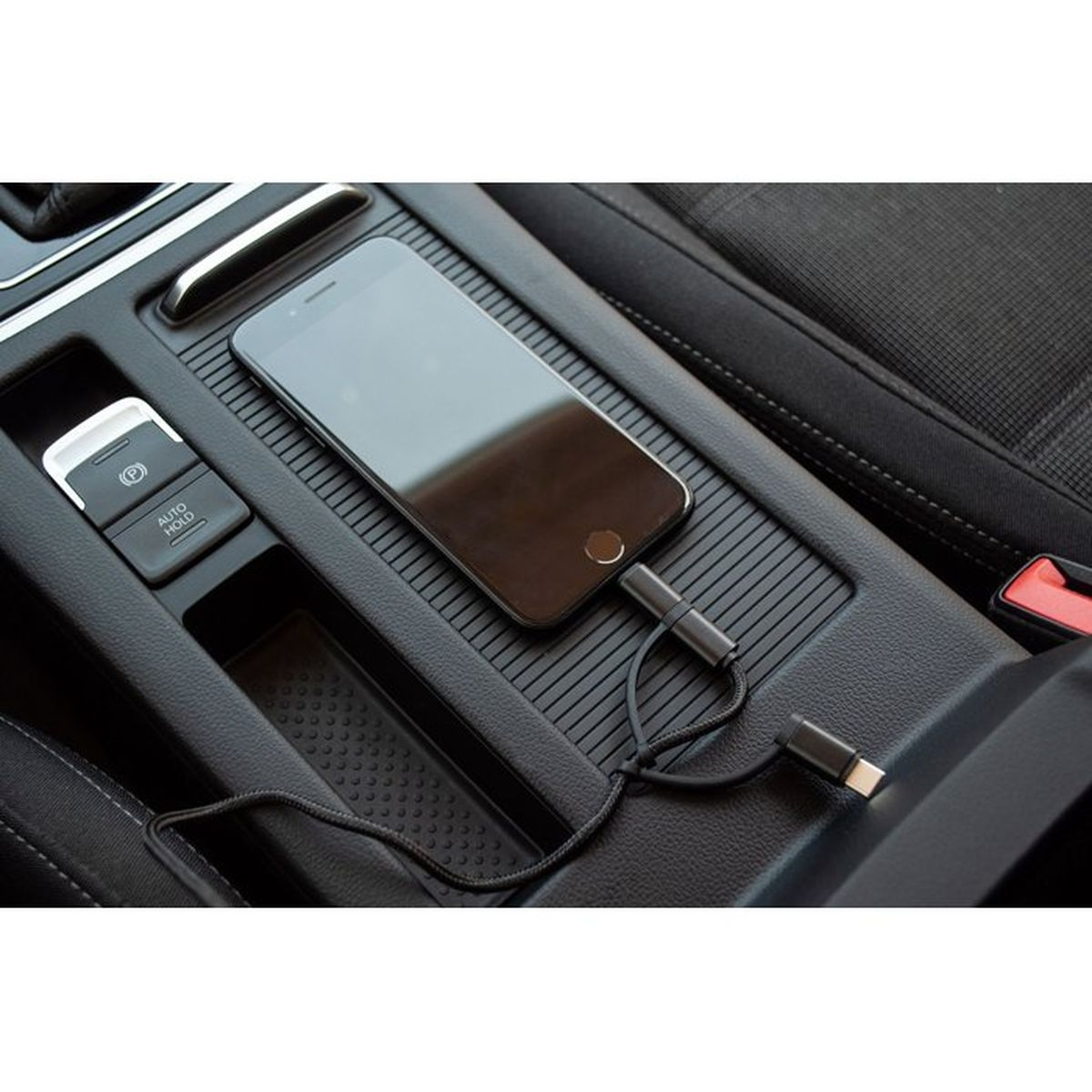 Ein Smartphone liegt in der Mittelkonsole eines Autos und ist mit einem schwarzen Ladekabel verbunden.