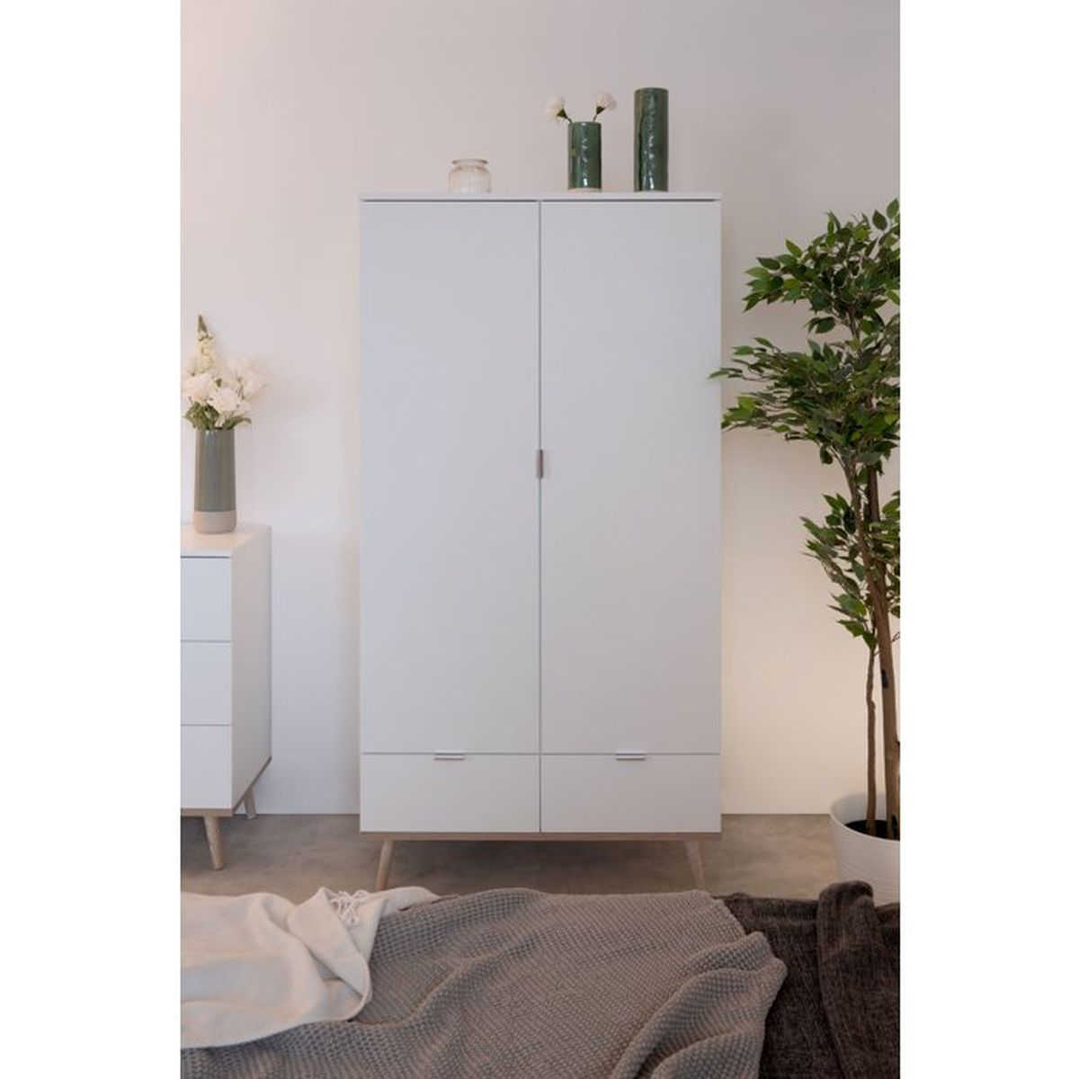 Ein weißer Schrank mit zwei Türen und zwei Schubladen steht in einem hellen Schlafzimmer.