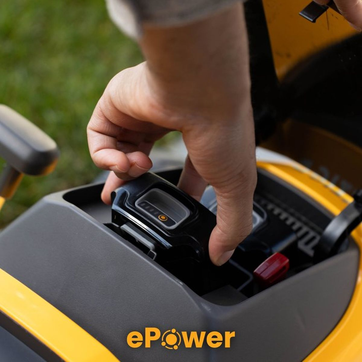 Eine Hand setzt eine schwarze Batterie in einen gelben Rasenmäher ein.