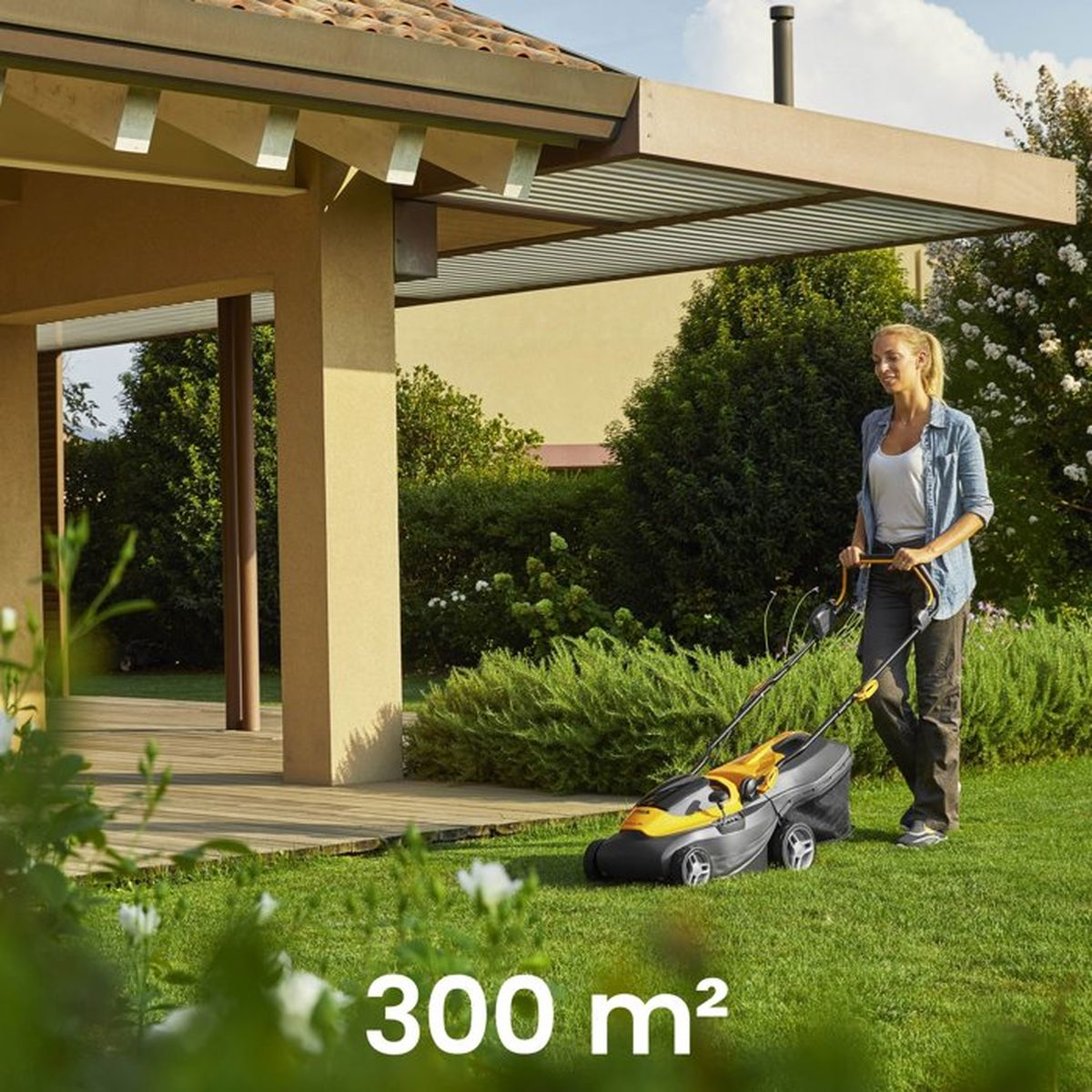 Eine Frau mäht den Rasen im Garten vor einem modernen Haus.