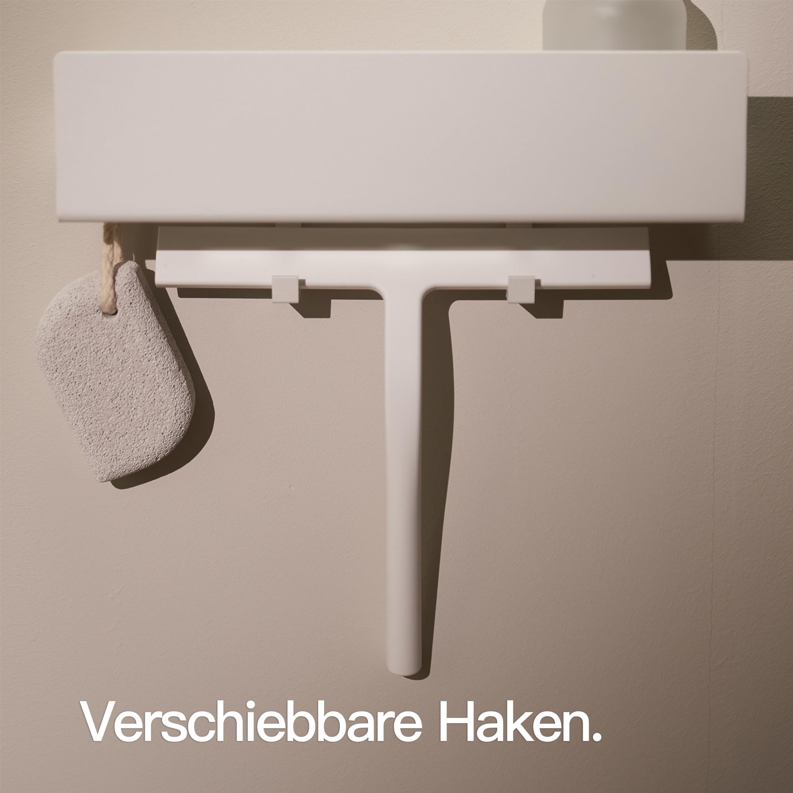 Ein weißer Duschabzieher hängt an einer Wandhalterung mit einem Bimsstein an der Seite.