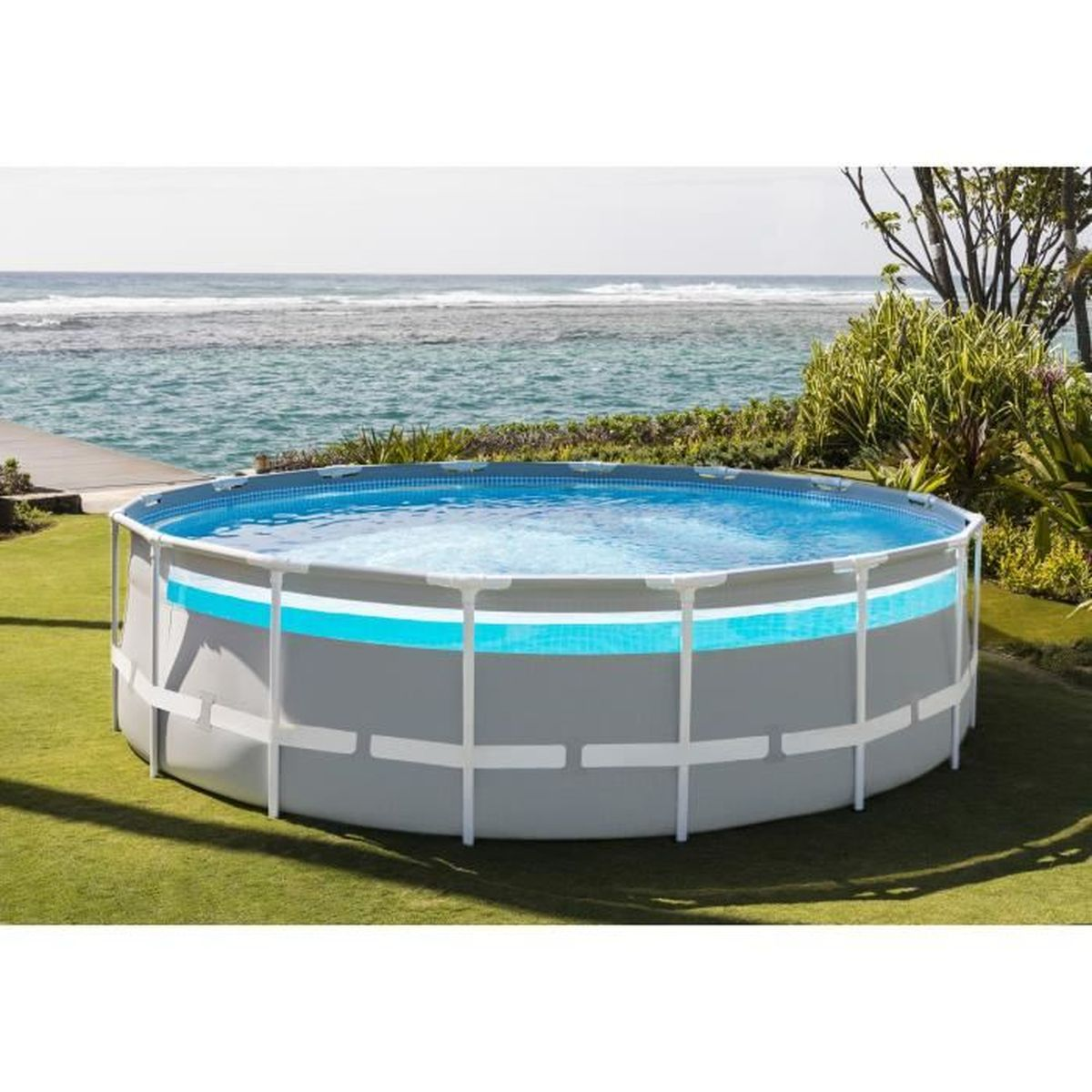Ein runder Aufstellpool mit weißem Rahmen auf grünem Rasen, im Hintergrund das blaue Meer.
