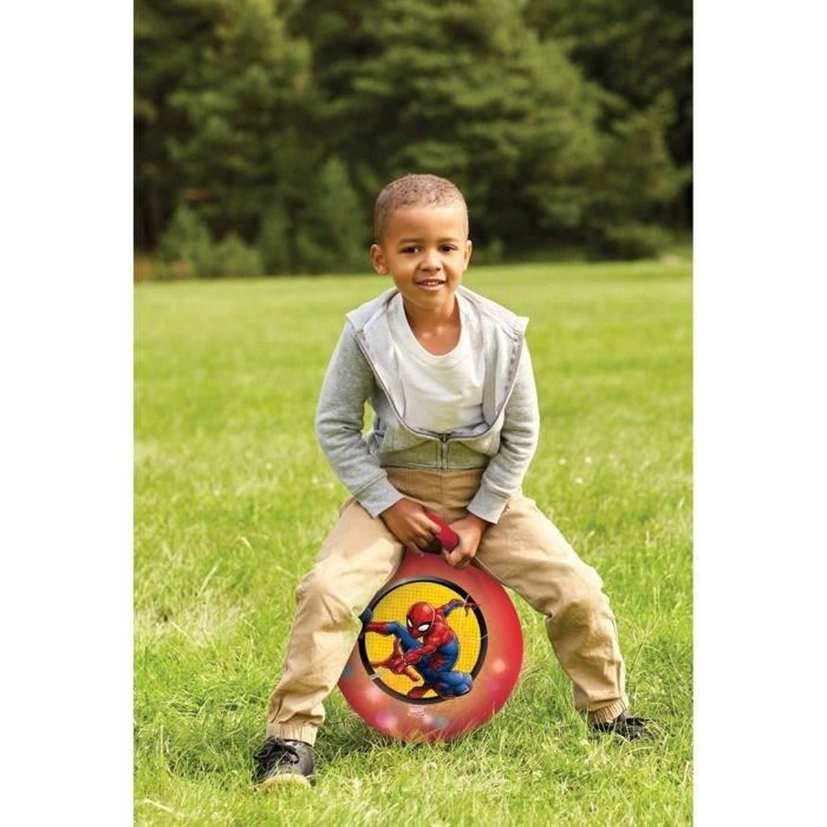 Ein junger Junge lächelt, während er auf einem roten Spider-Man-Hüpfball im Park hüpft.