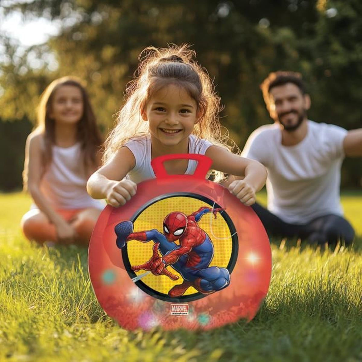 Ein lächelndes Mädchen hält in einem Park eine rote Spider-Man-Scheibe, im Hintergrund Mann und Mädchen.