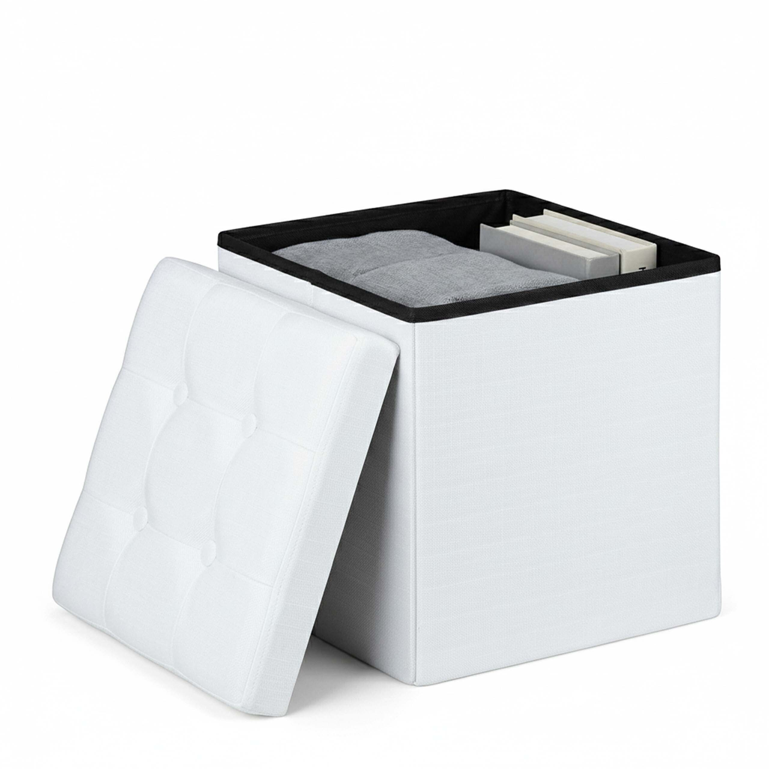 Ein weißer, quadratischer Hocker mit abnehmbarem gepolstertem Deckel, gefüllt mit Büchern und einer Decke vor weißem Hintergrund.