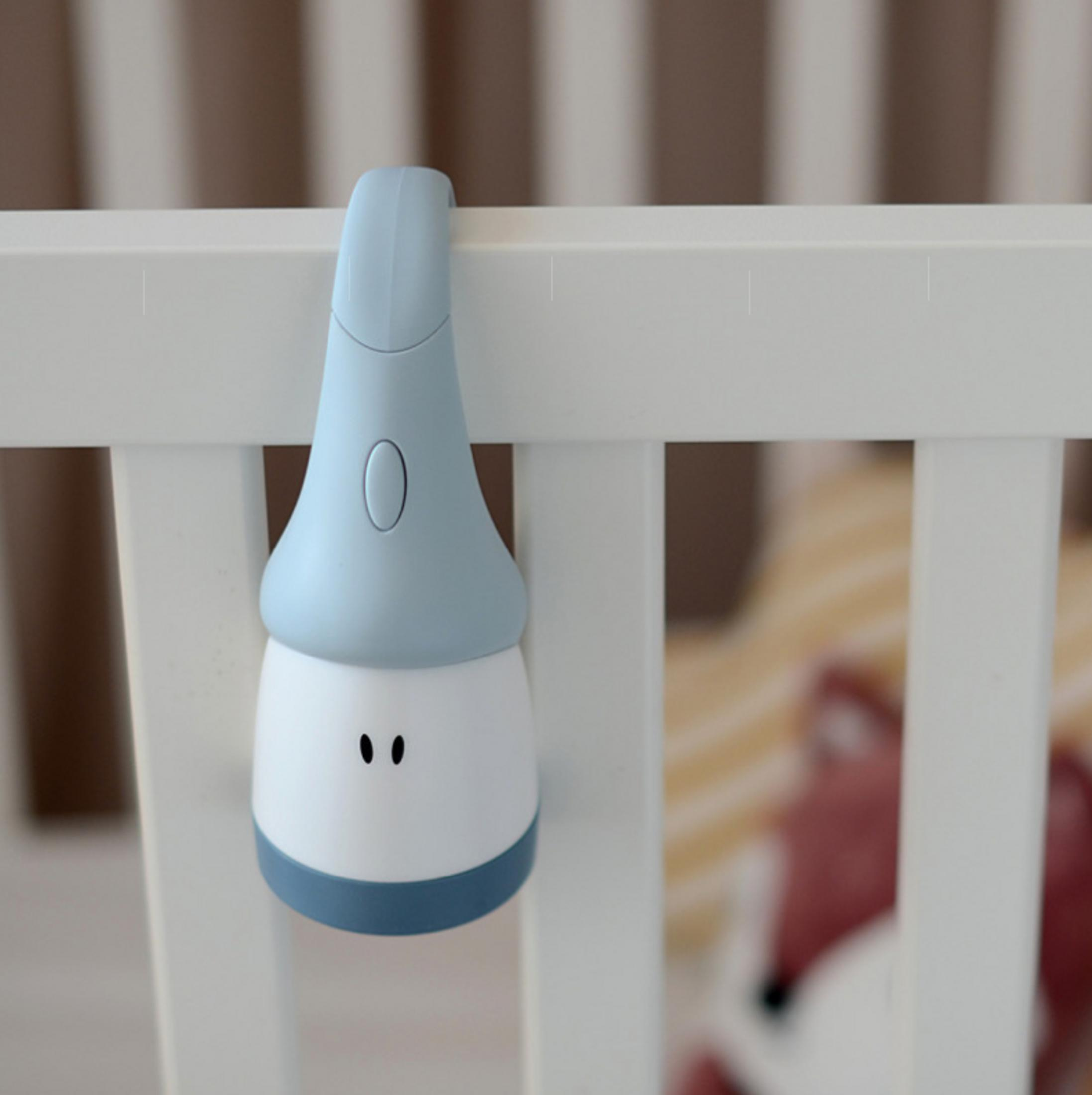 Eine blaue und weiße Nachtlampe mit süßem Gesicht hängt an einer weißen Babybettgitter.