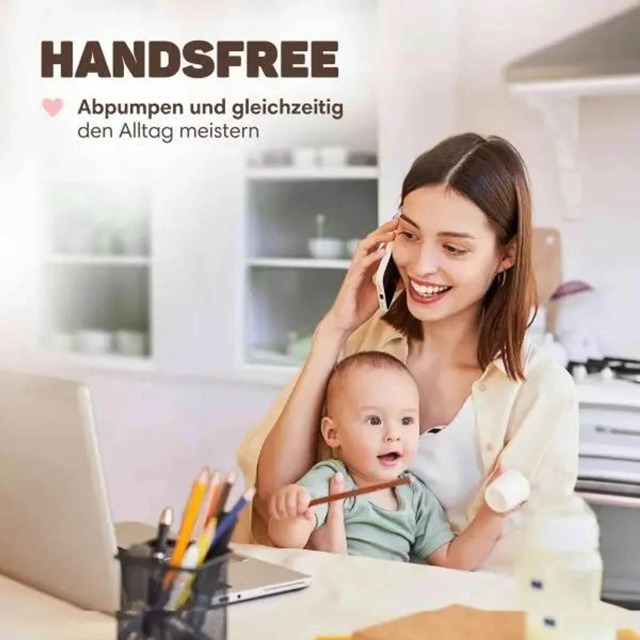 Lächelnte Mutter hält Baby und telefoniert bei der Arbeit am Laptop in der Küche.