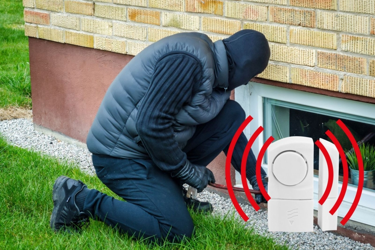 Ein Einbrecher in Schwarz versucht neben einem Alarmsensor in ein Fenster einzudringen.