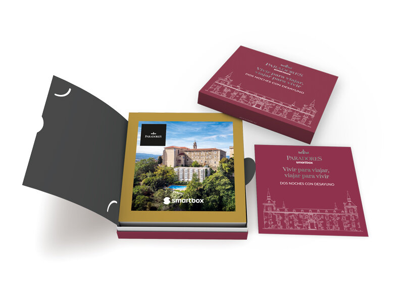 Una caja de regalo roja abierta muestra un álbum de fotos con un edificio histórico y una tarjeta.
