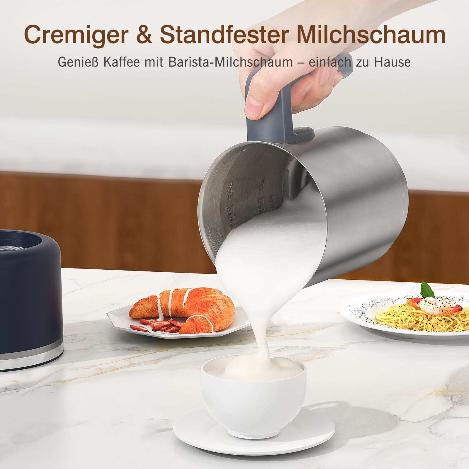 Main verse de la mousse de lait d'un pichet dans une tasse sur table en marbre, avec croissant et pâtes.