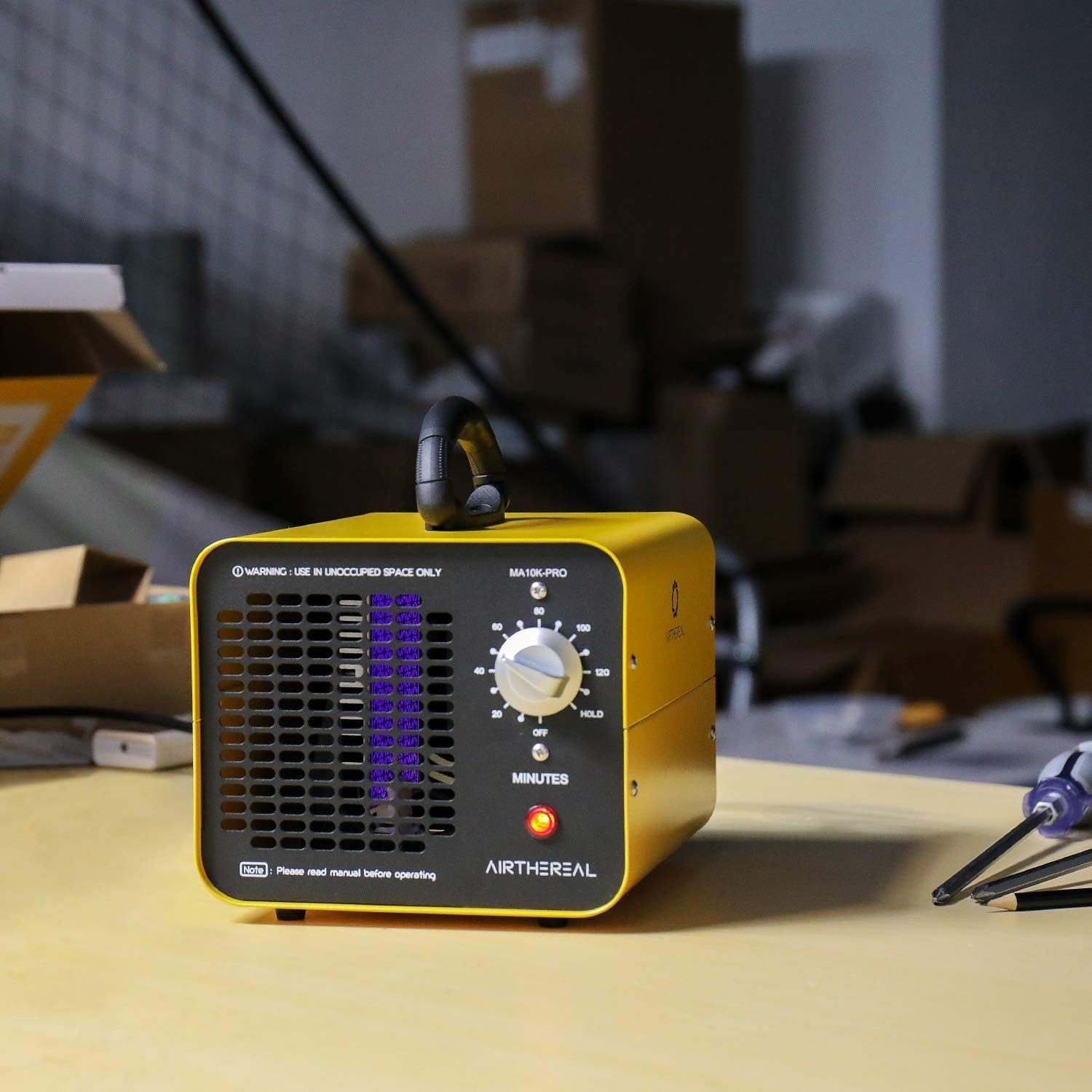 Ein gelber Airthereal Ozongenerator mit schwarzem Griff und Zeitschaltuhr steht auf einem Tisch in einem Raum.
