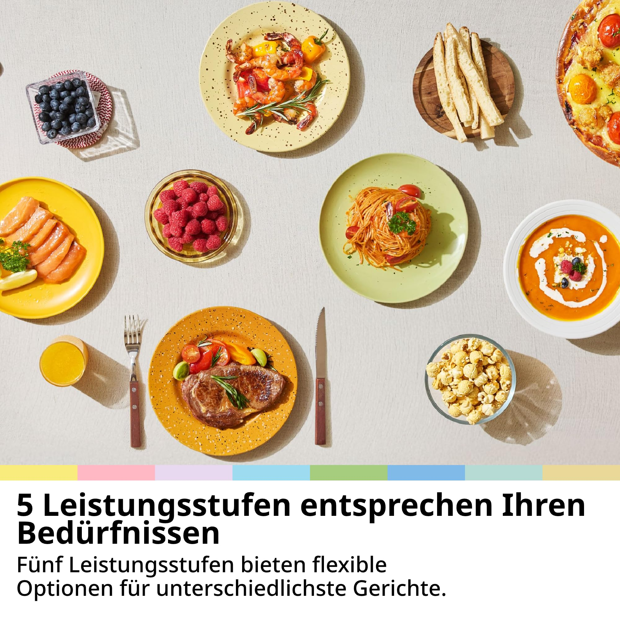Verschiedene Gerichte auf einem Tisch angeordnet, darunter Suppe, Steak, Pasta, Pizza und Beeren.