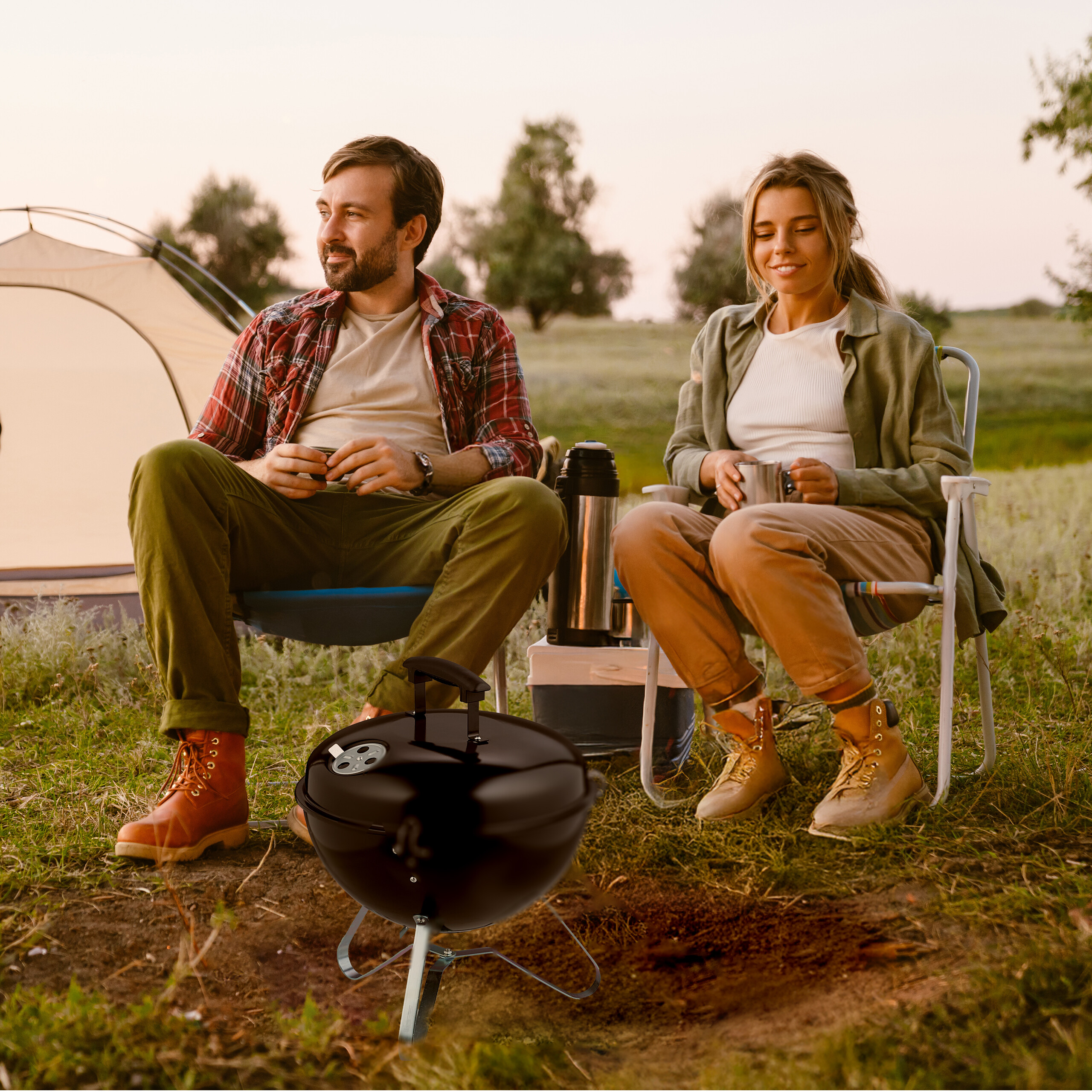 Ein Paar entspannt auf Campingstühlen in der Nähe eines Zeltes und eines Grills auf einer Wiese.