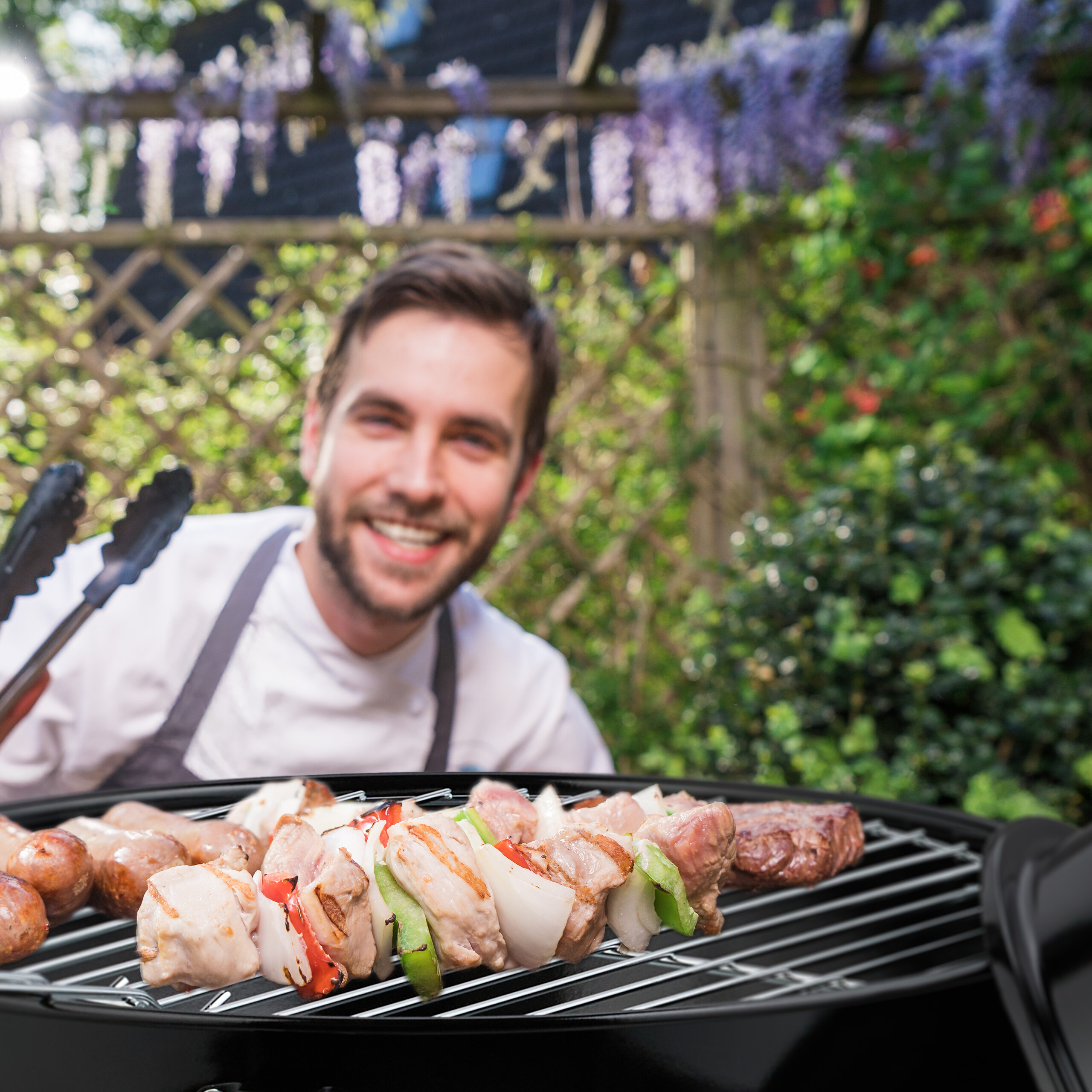 Ein lächelnder Koch grillt Fleisch und Gemüse auf einem Barbecue im Freien.