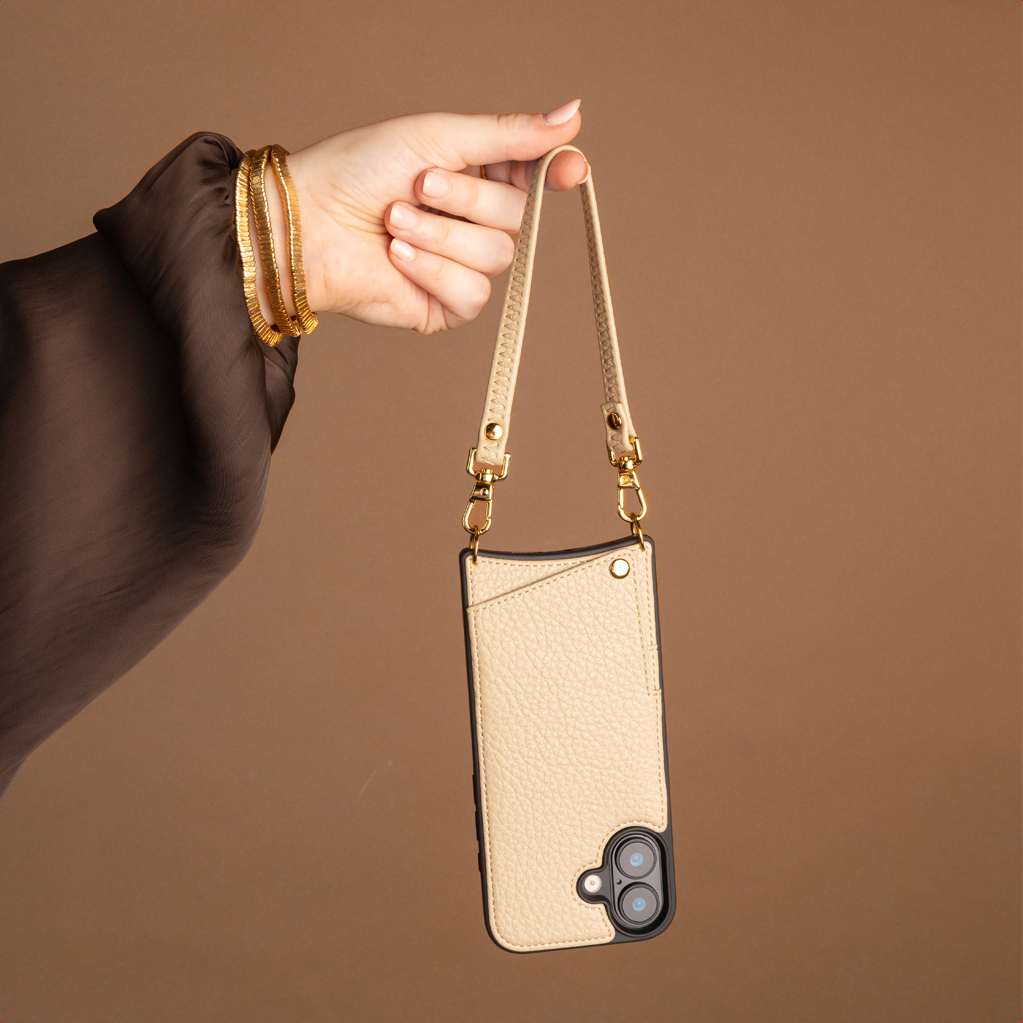Eine Person hält eine beige Handyhülle mit Band vor braunem Hintergrund.