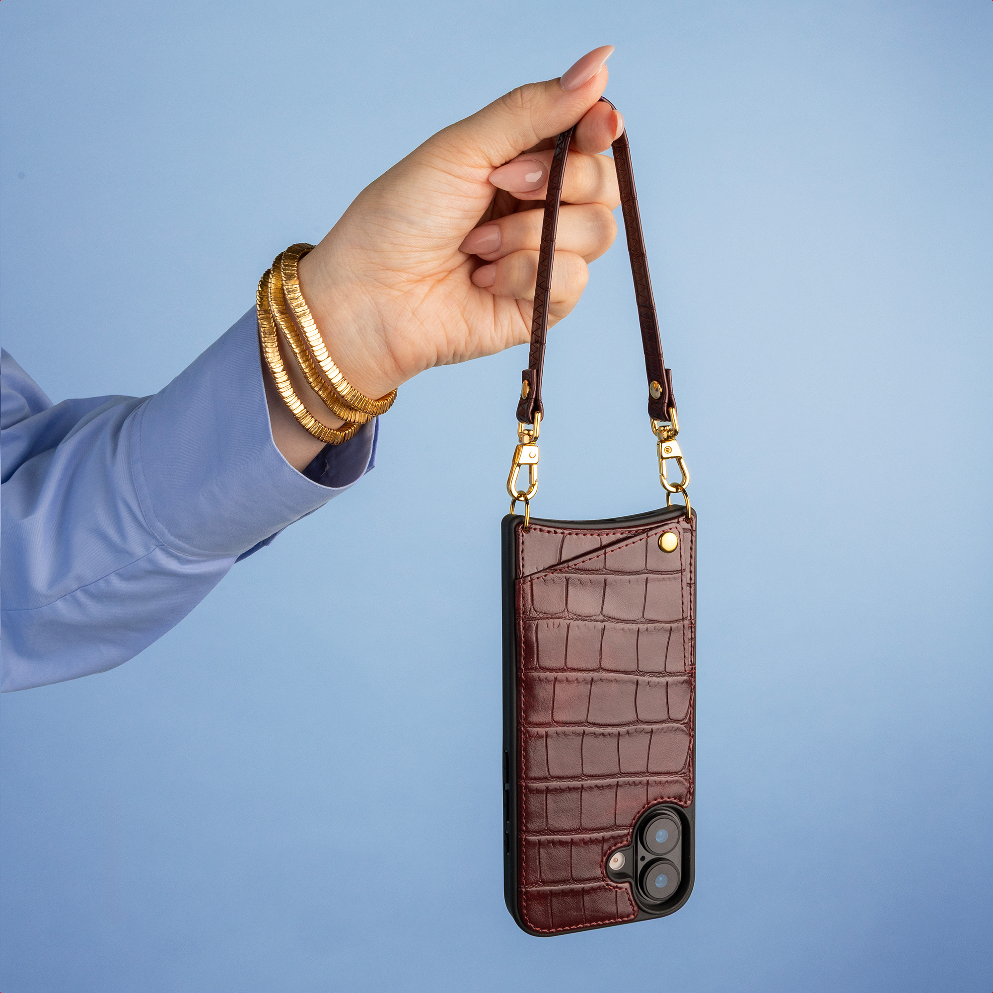 A hand holds a brown leather phone case with a strap against a blue background.