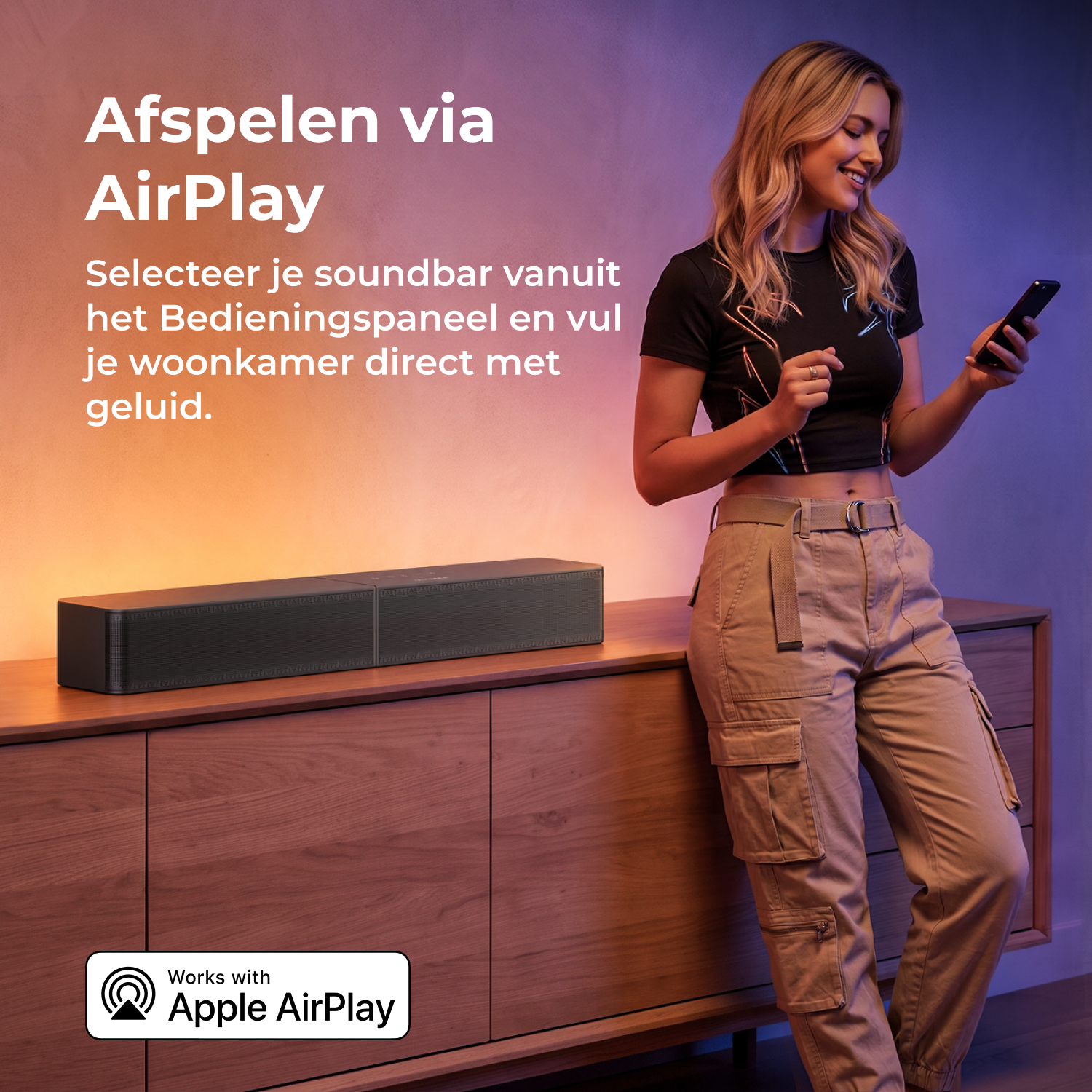 Een blonde vrouw leunt tegen een houten kast met soundbar en gebruikt haar smartphone voor een gekleurde muur.