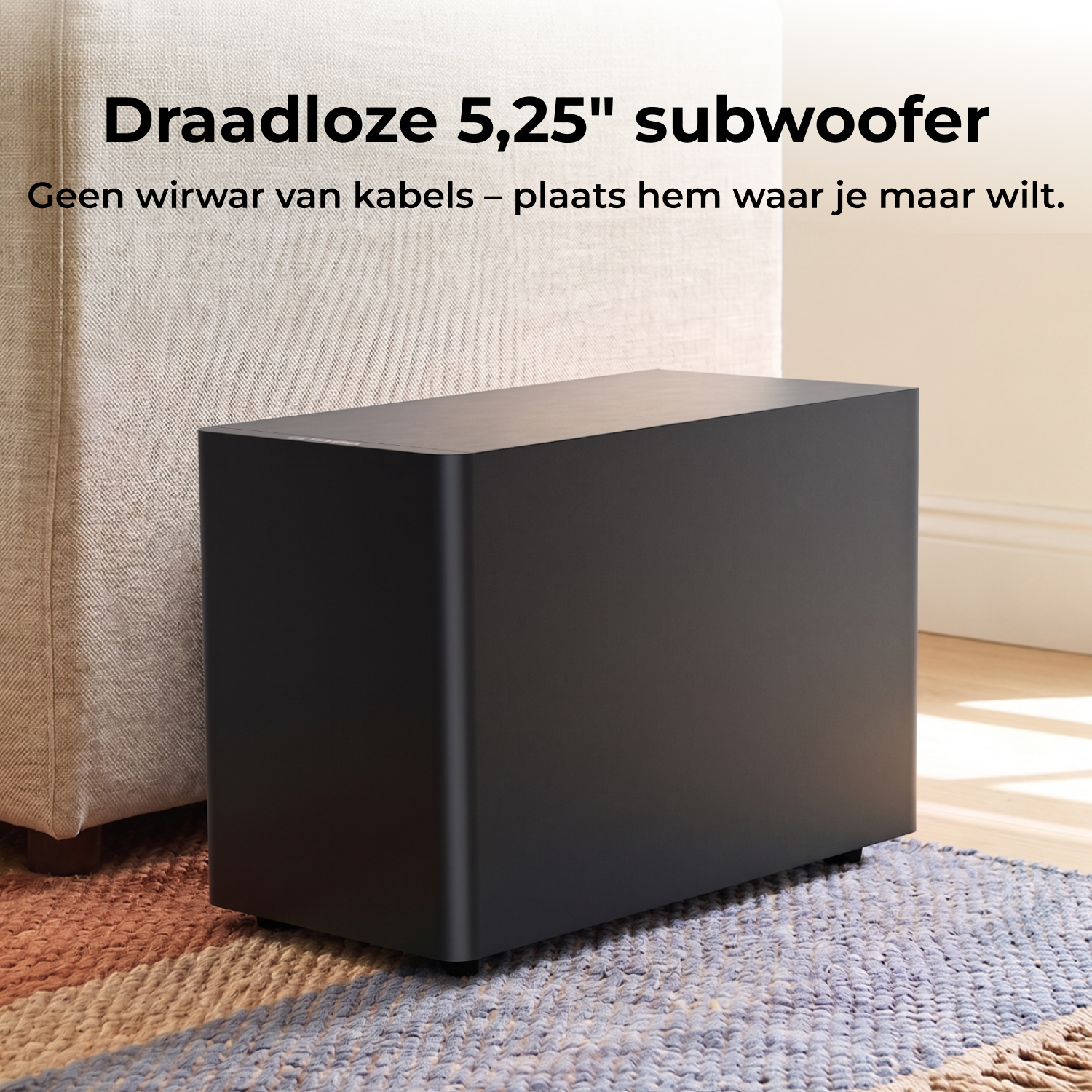 Een zwarte draadloze subwoofer staat op een kleed naast een bank.