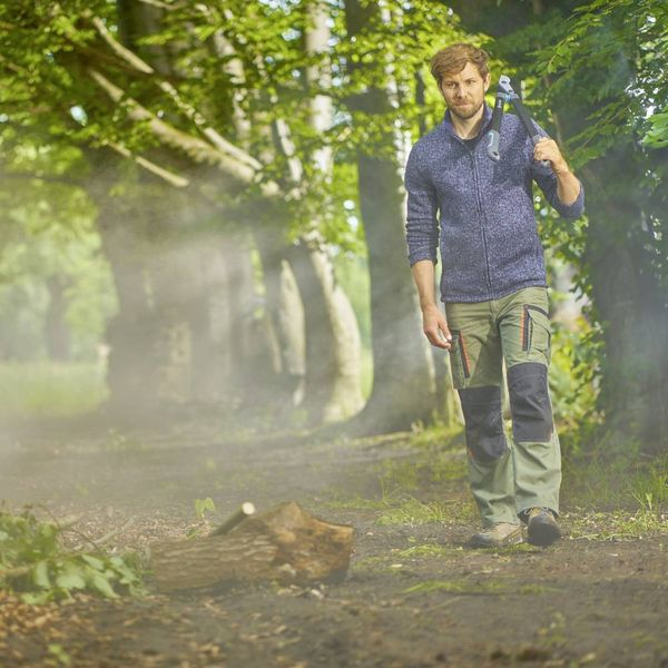 Ein Mann geht durch einen sonnigen Wald und trägt eine Axt über der Schulter.