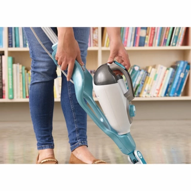 Una donna con jeans blu tiene un aspirapolvere bianco e blu davanti a una libreria.