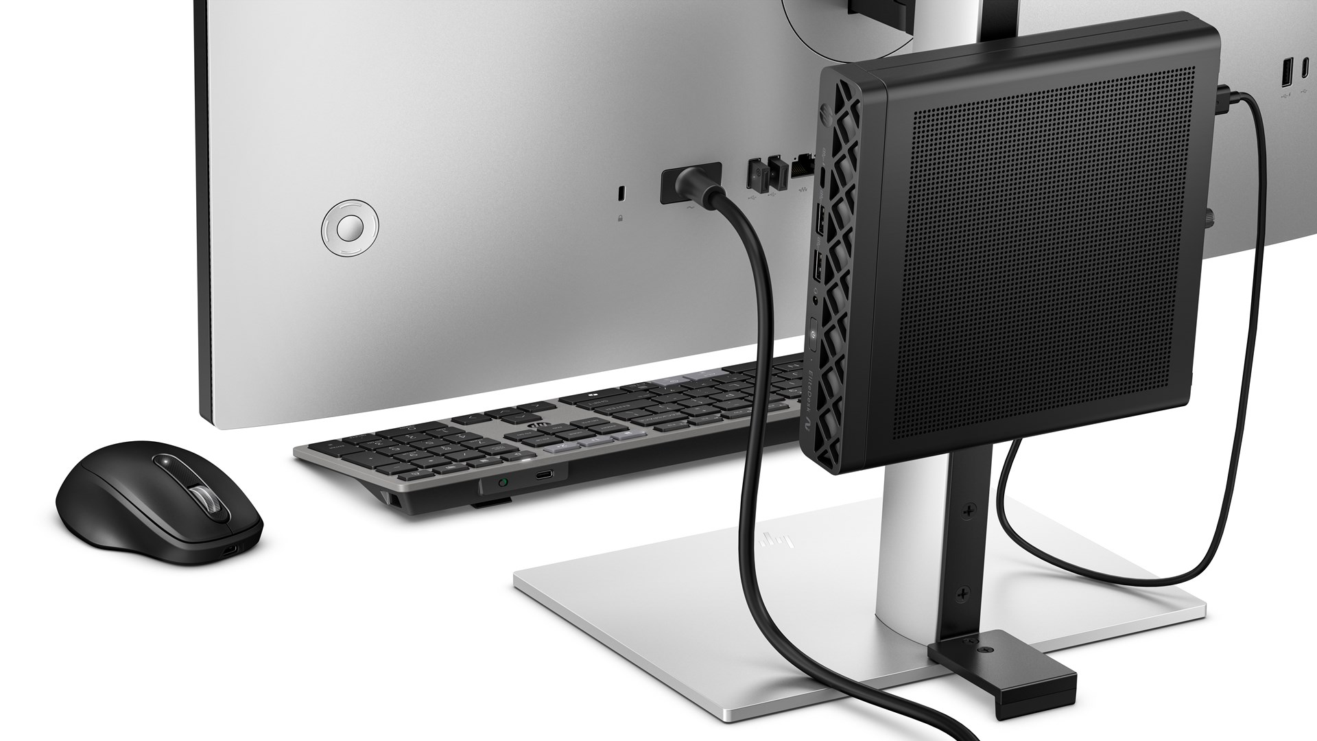 Czarny mini PC na stojaku monitora, z klawiaturą i myszą na białym biurku.