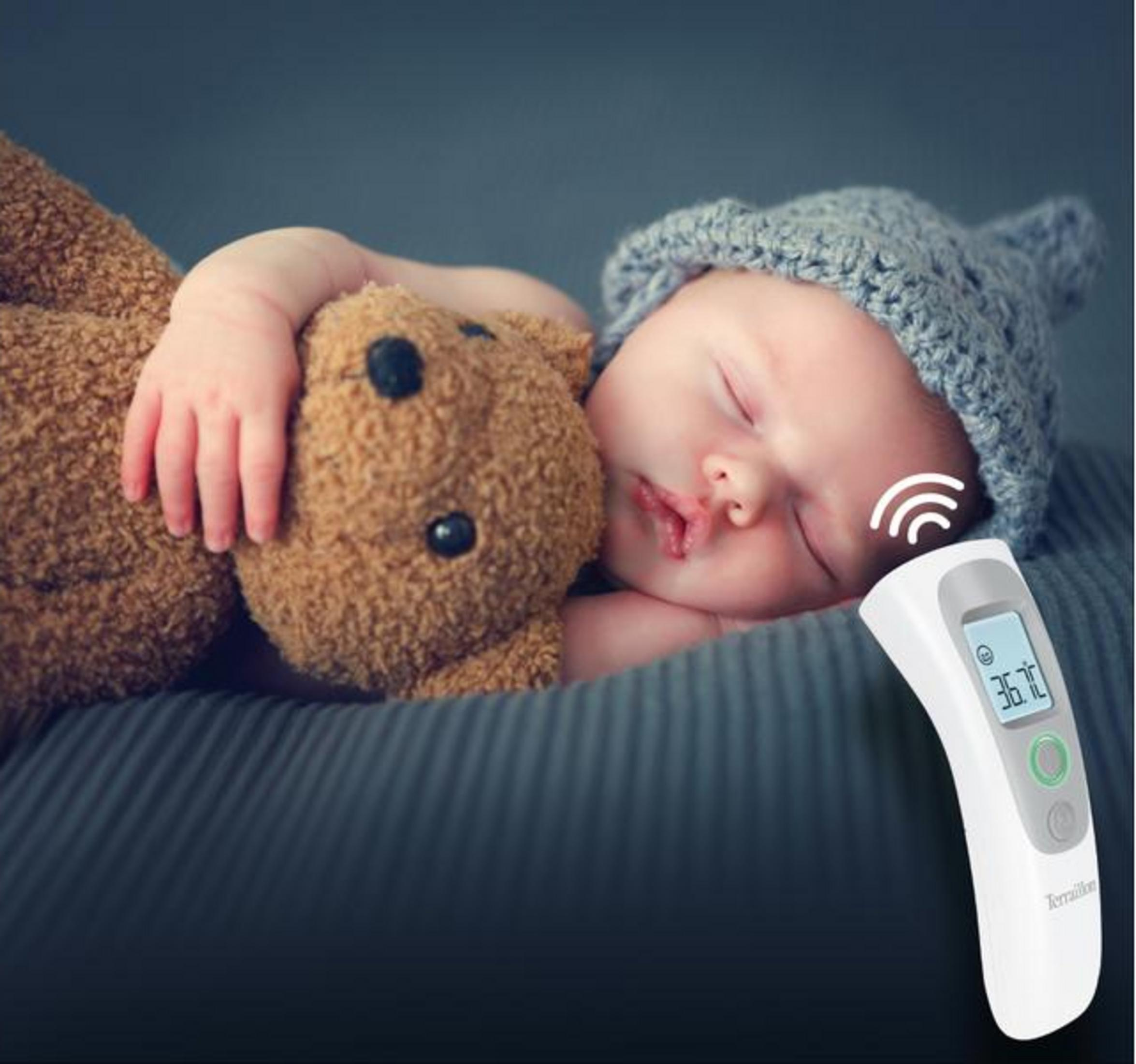 Ein schlafendes Baby mit grauer Mütze umarmt einen Teddybären, während ein Thermometer misst.