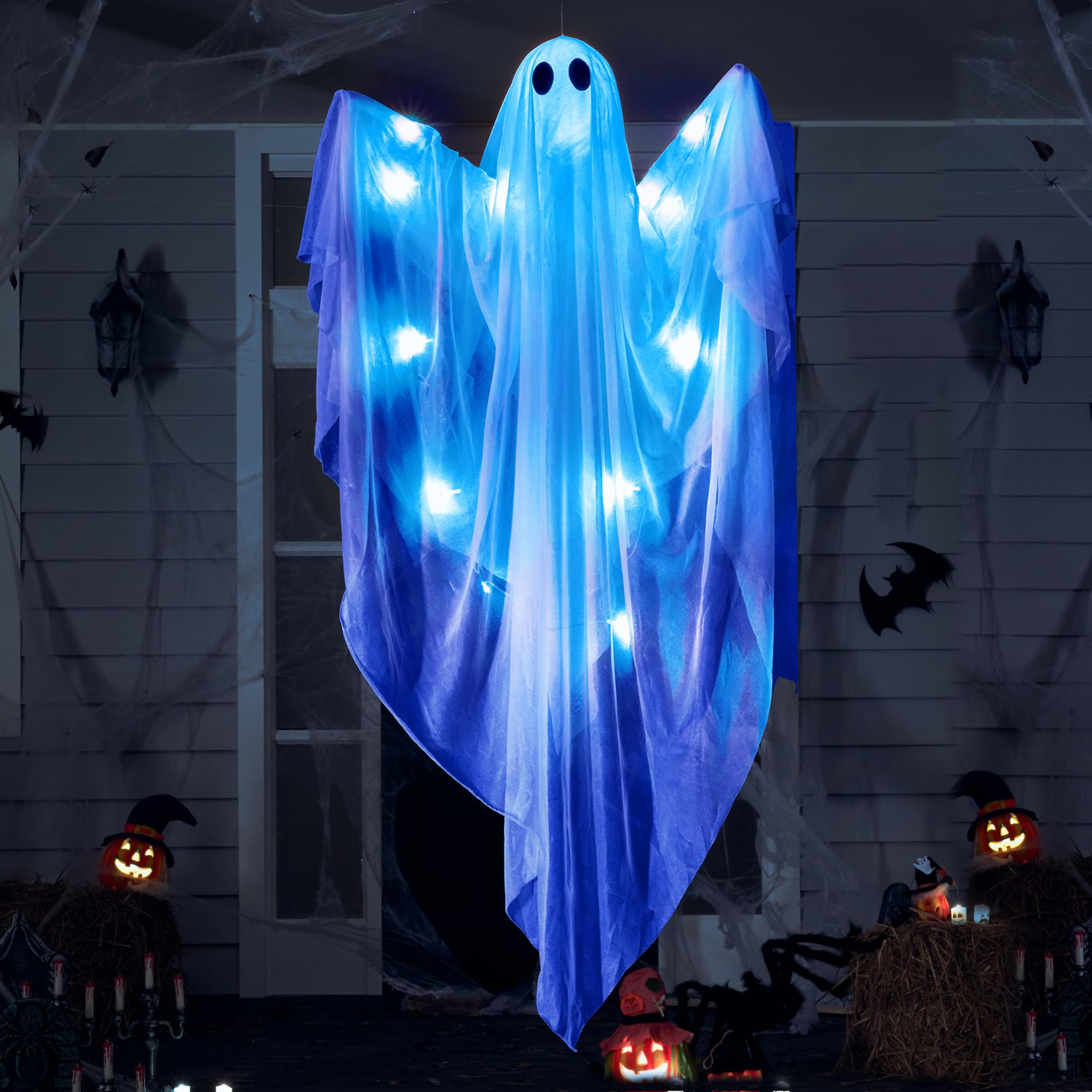 Ein leuchtender, blau beleuchteter Hängegeist vor einem Halloween-dekorierten Haus mit Kürbissen.