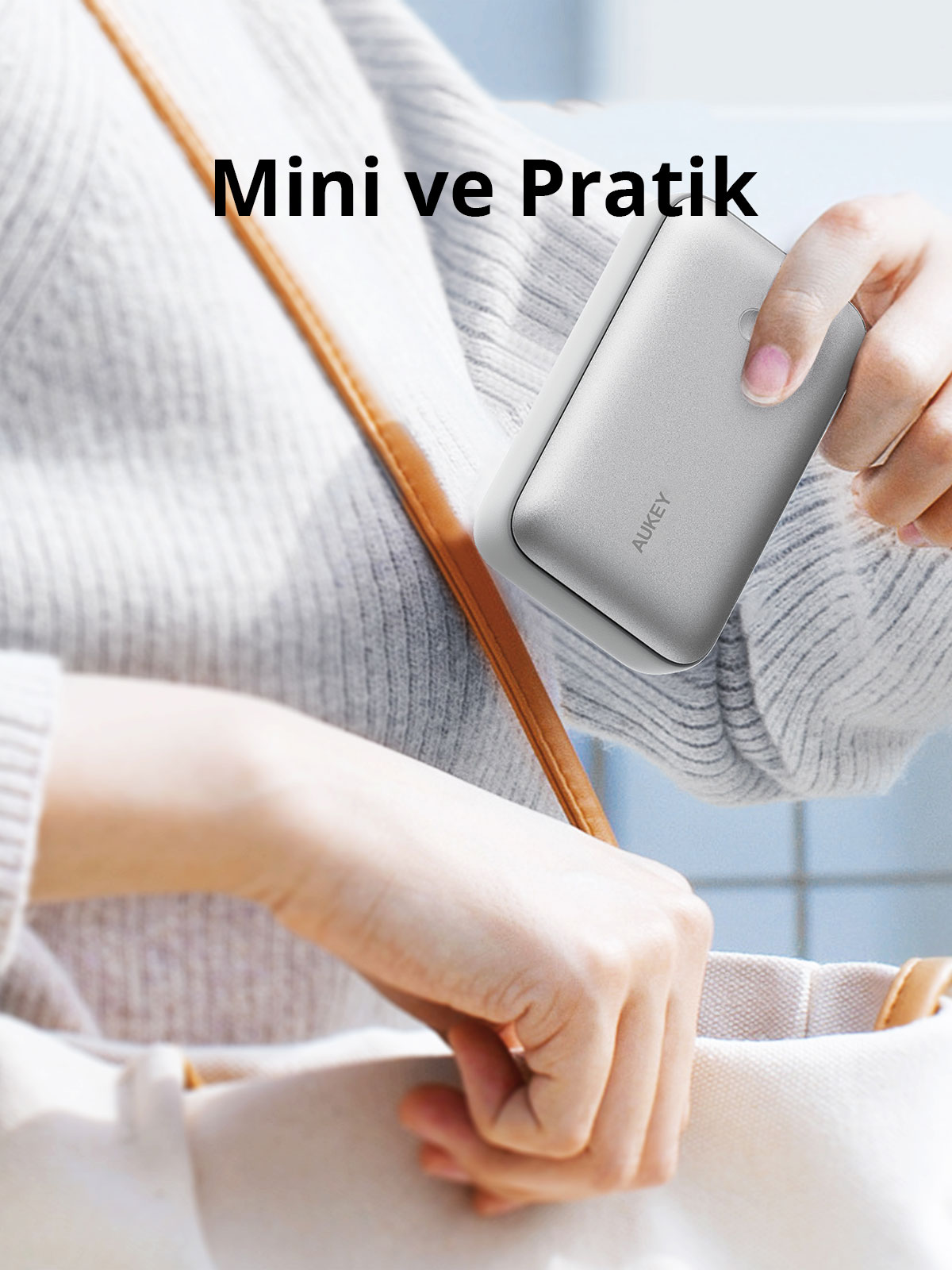 Bir kişi çantasından gri renkli AUKEY powerbank çıkarıyor.