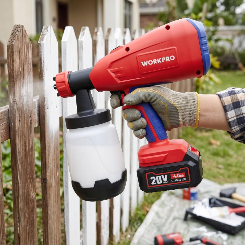 Bir kişi kırmızı bir Workpro kablosuz boya tabancasıyla ahşap çiti boyuyor.