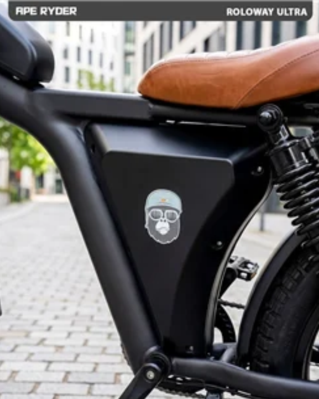 Kahverengi deri seleli ve bataryasında goril çıkartması olan siyah Ape Ryder Roloway Ultra e-bike.