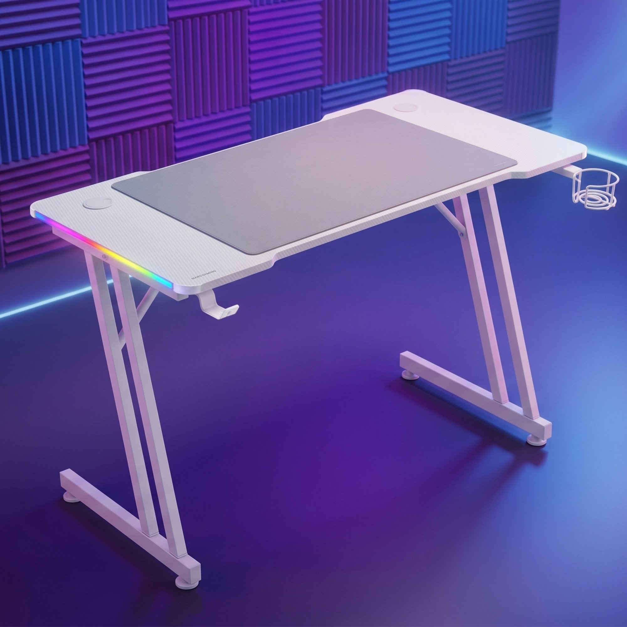 Escritorio gaming blanco con luces LED, alfombrilla gris y portavasos, frente a paneles acústicos azules.