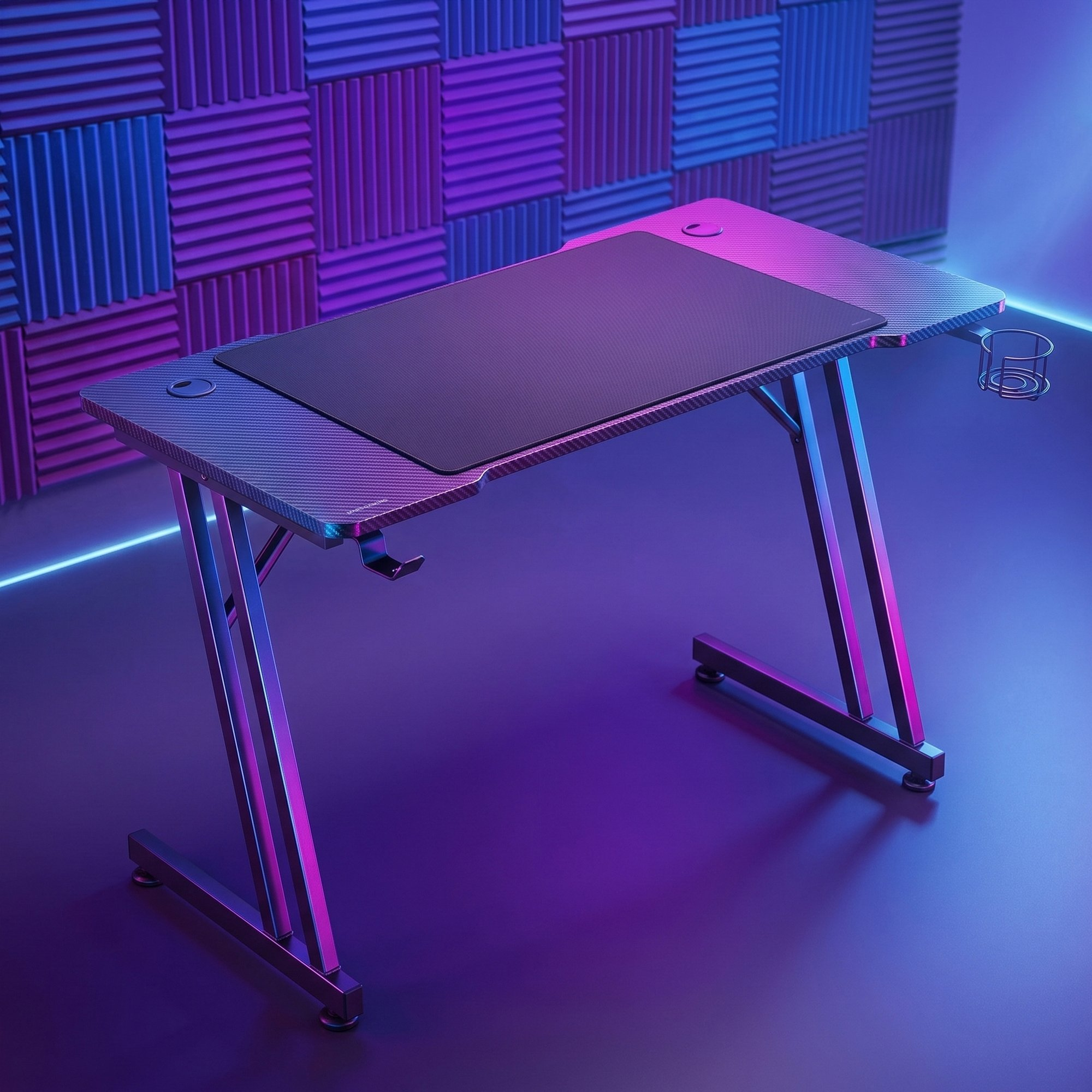 Escritorio gaming moderno con patas en Z y alfombrilla negra frente a pared acústica azul.