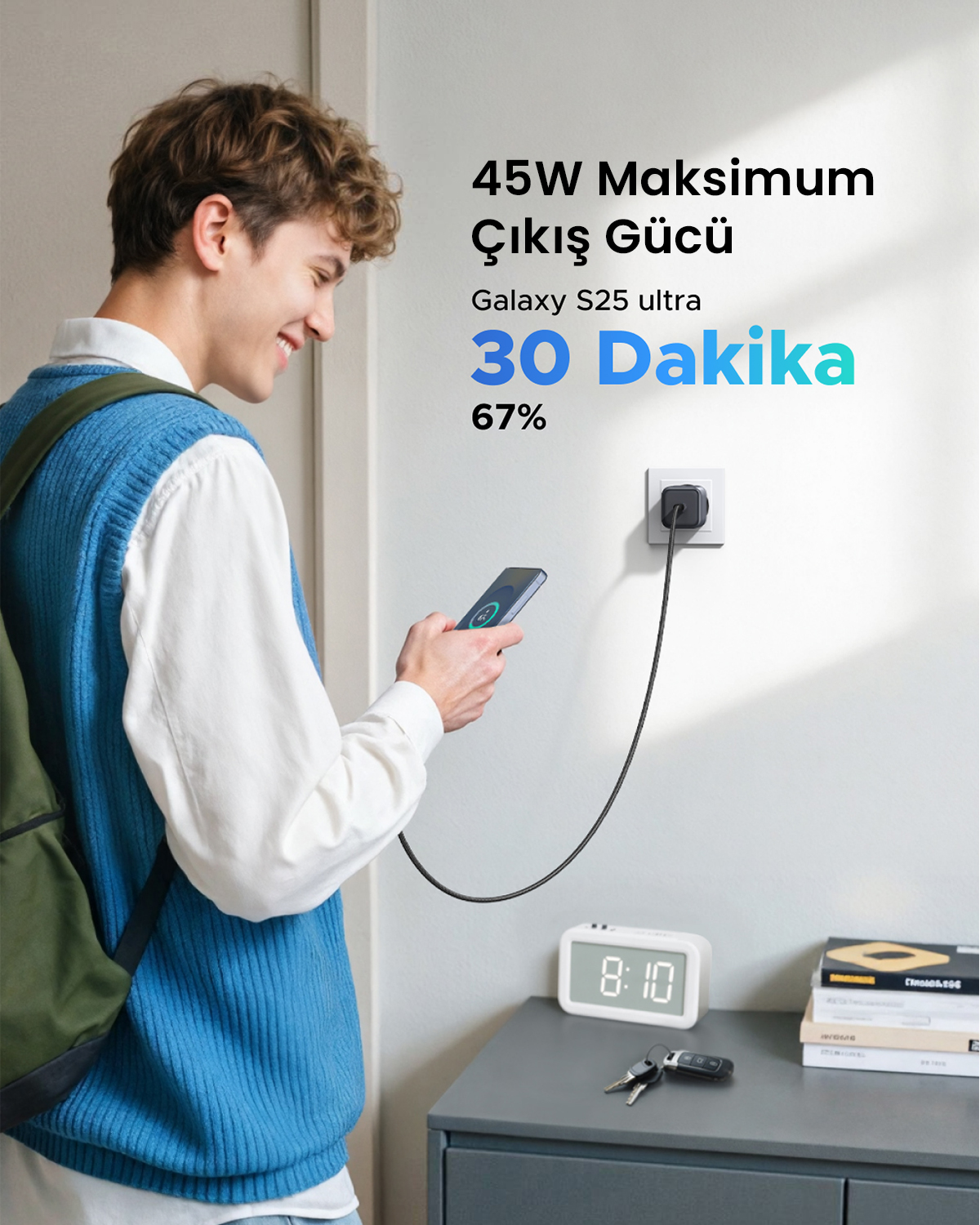 Genç bir adam, duvardaki şarja takılı olan akıllı telefonunu tutarken gülümsüyor.