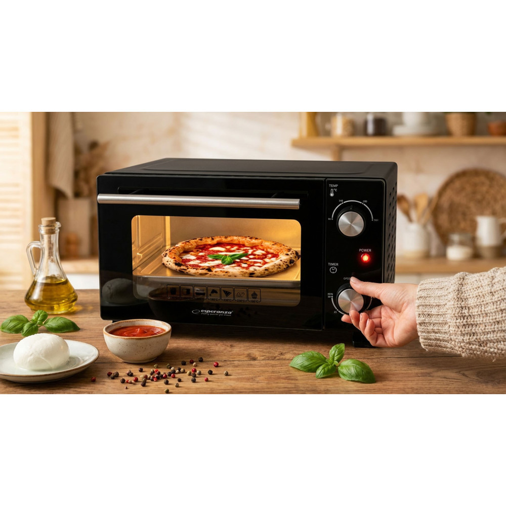 Ręka reguluje czarny mini piekarnik piekący pizzę, stojący na drewnianym blacie z składnikami.