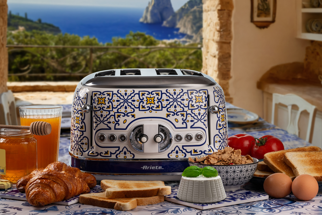 Ein blau-weiß gemusterter Toaster steht auf einem gedeckten Tisch mit Frühstückszutaten und Meerblick im Hintergrund.