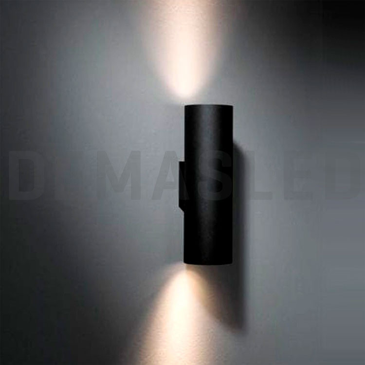 Una lámpara de pared cilíndrica negra montada en una pared gris, proyectando luz hacia arriba y hacia abajo.
