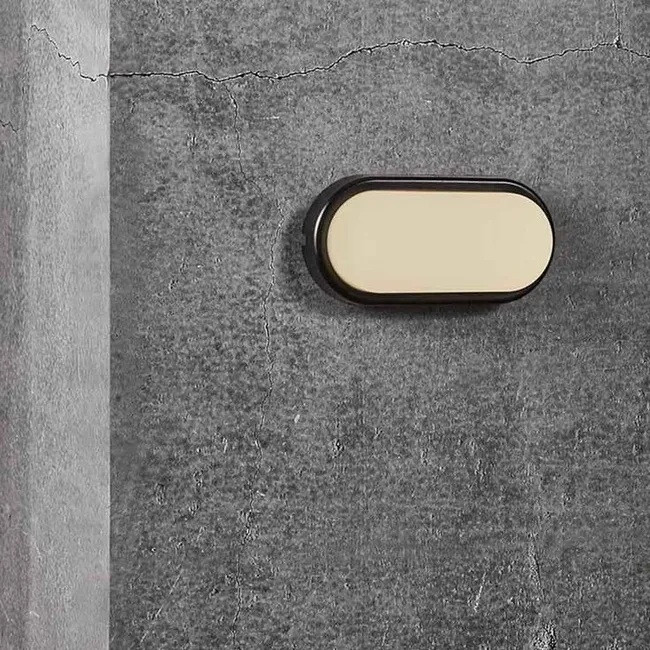 Una lámpara de pared ovalada negra con un inserto claro en una pared de hormigón gris.