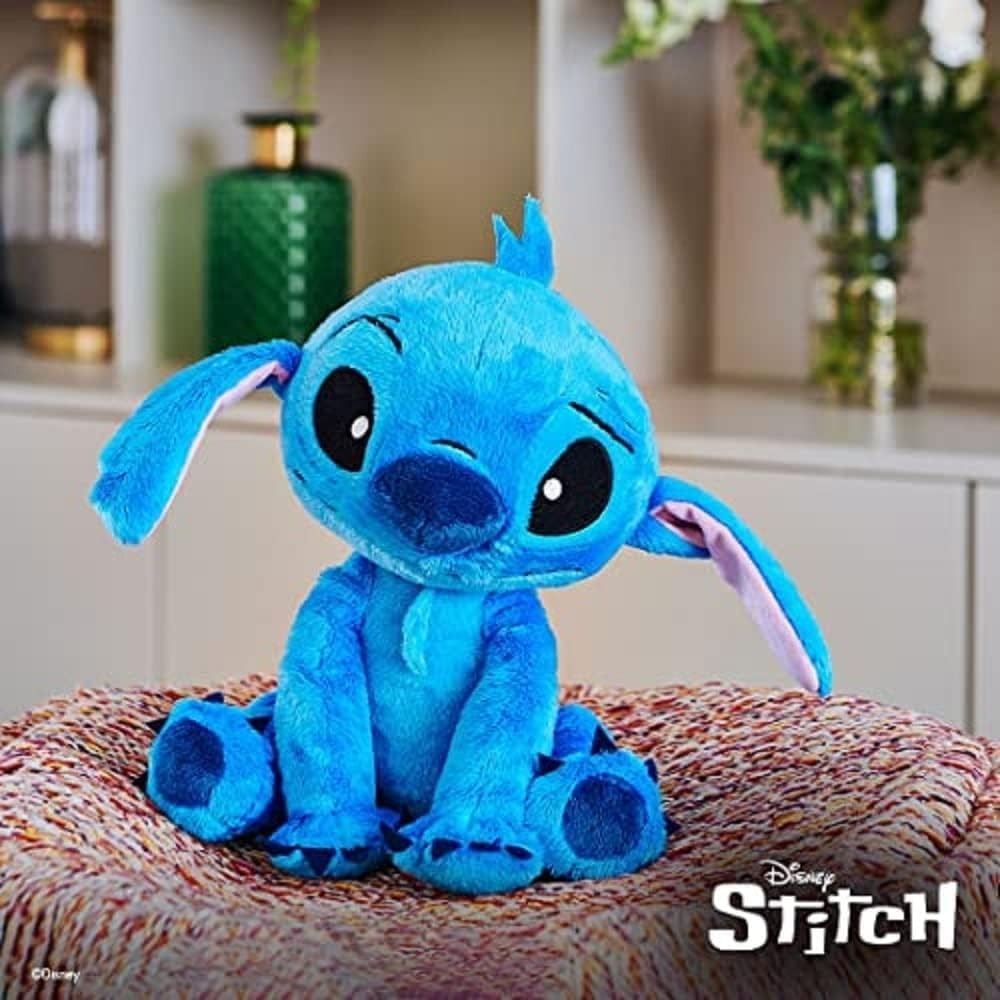 Peluche azul de Stitch sentado en una manta estampada frente a una estantería.
