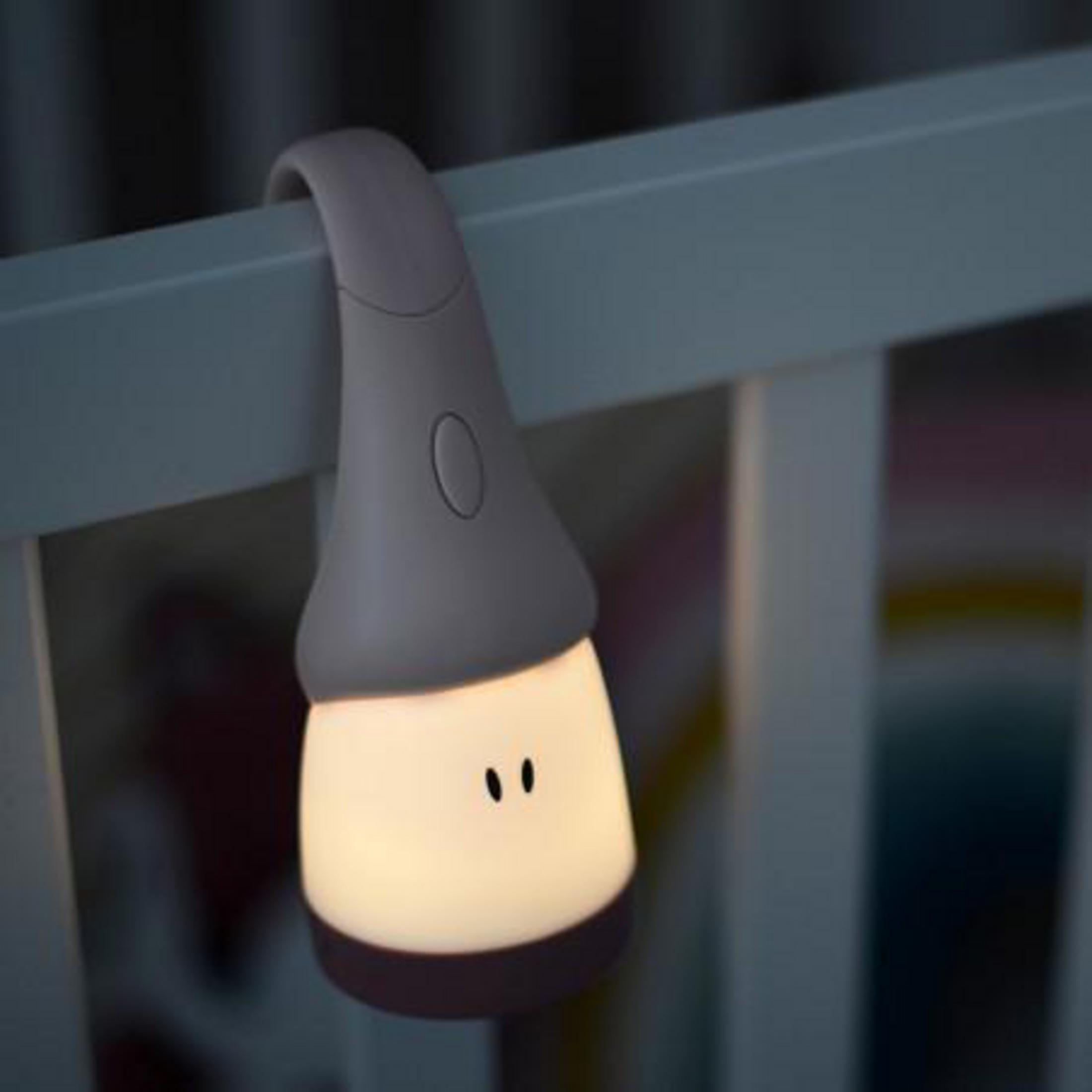 Eine kleine, graue Nachtlampe in Figurenform hängt am Rand eines Kinderbetts und strahlt ein warmes Licht aus.