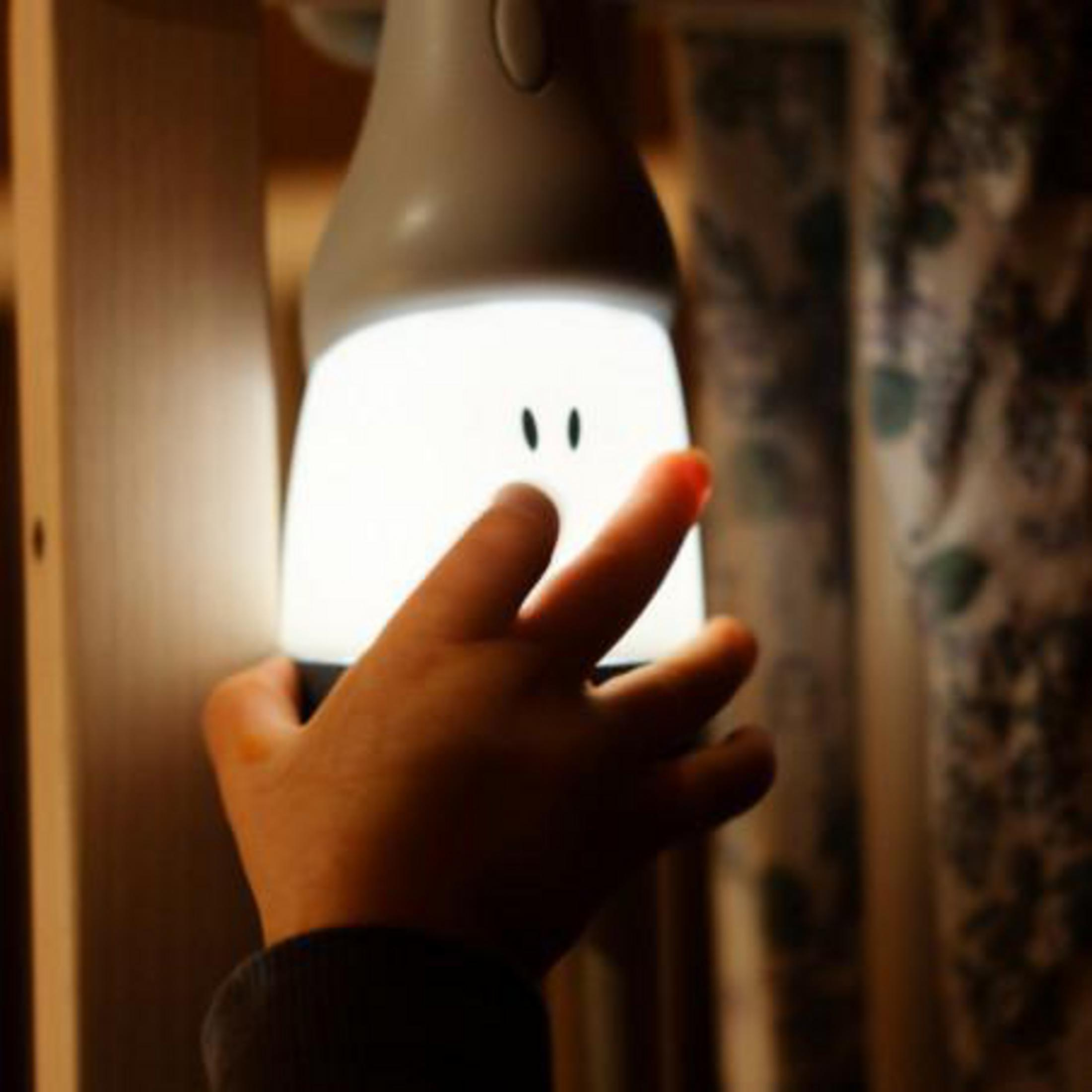 Ein Kinderhand berührt eine niedliche, leuchtende Nachtlampe mit kleinen Augen.