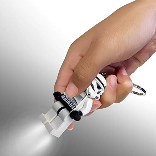 Una mano sostiene una linterna de llavero Lego Stormtrooper brillante contra un fondo gris.